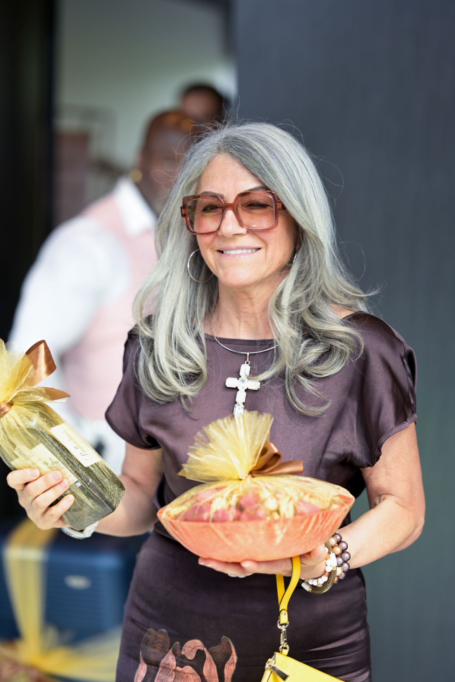 Person wearing sunglasses and purple dress holding decorative yellow packages.