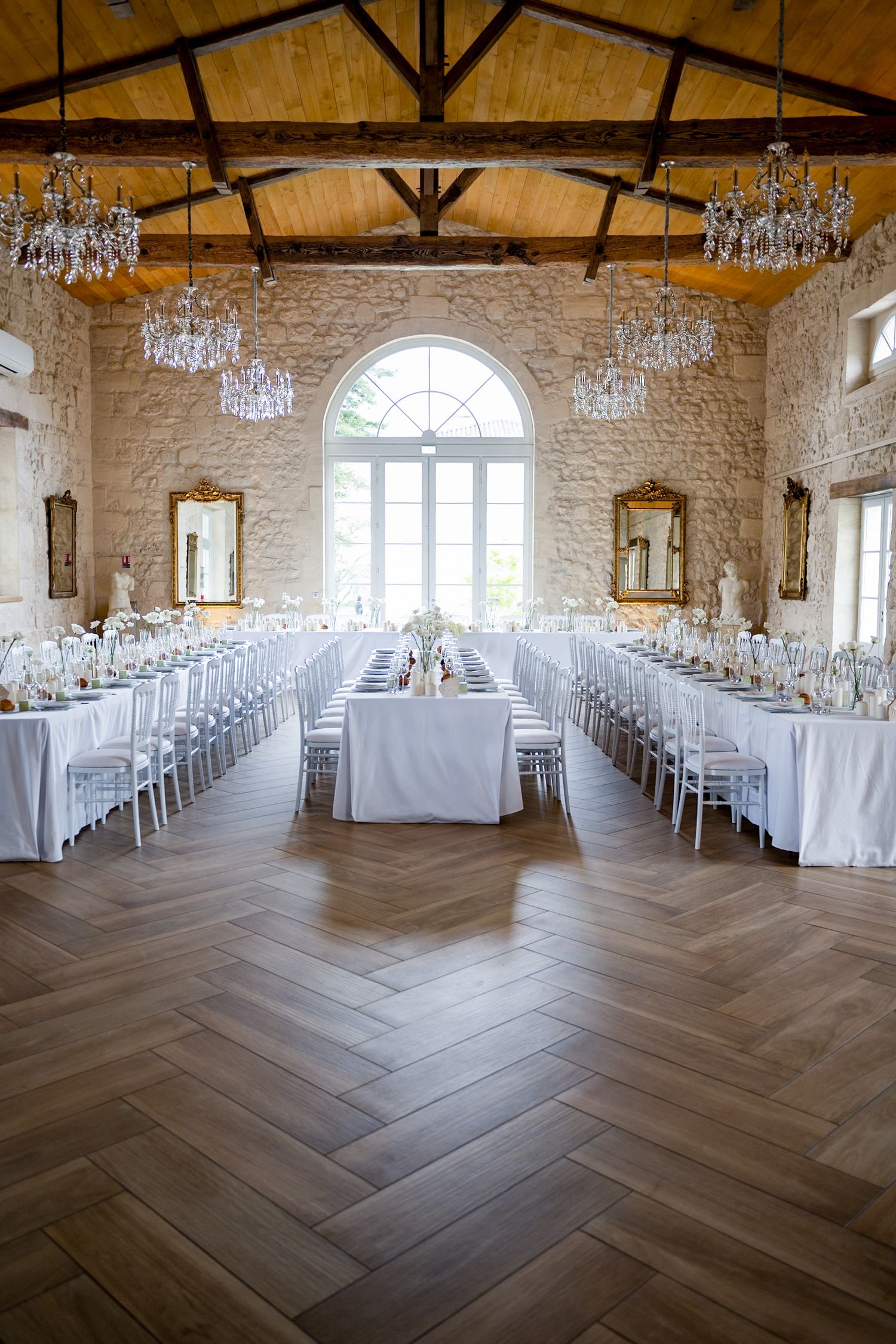 An elegant wedding reception hall with crystal chandeliers and herringbone floors set for dinner.