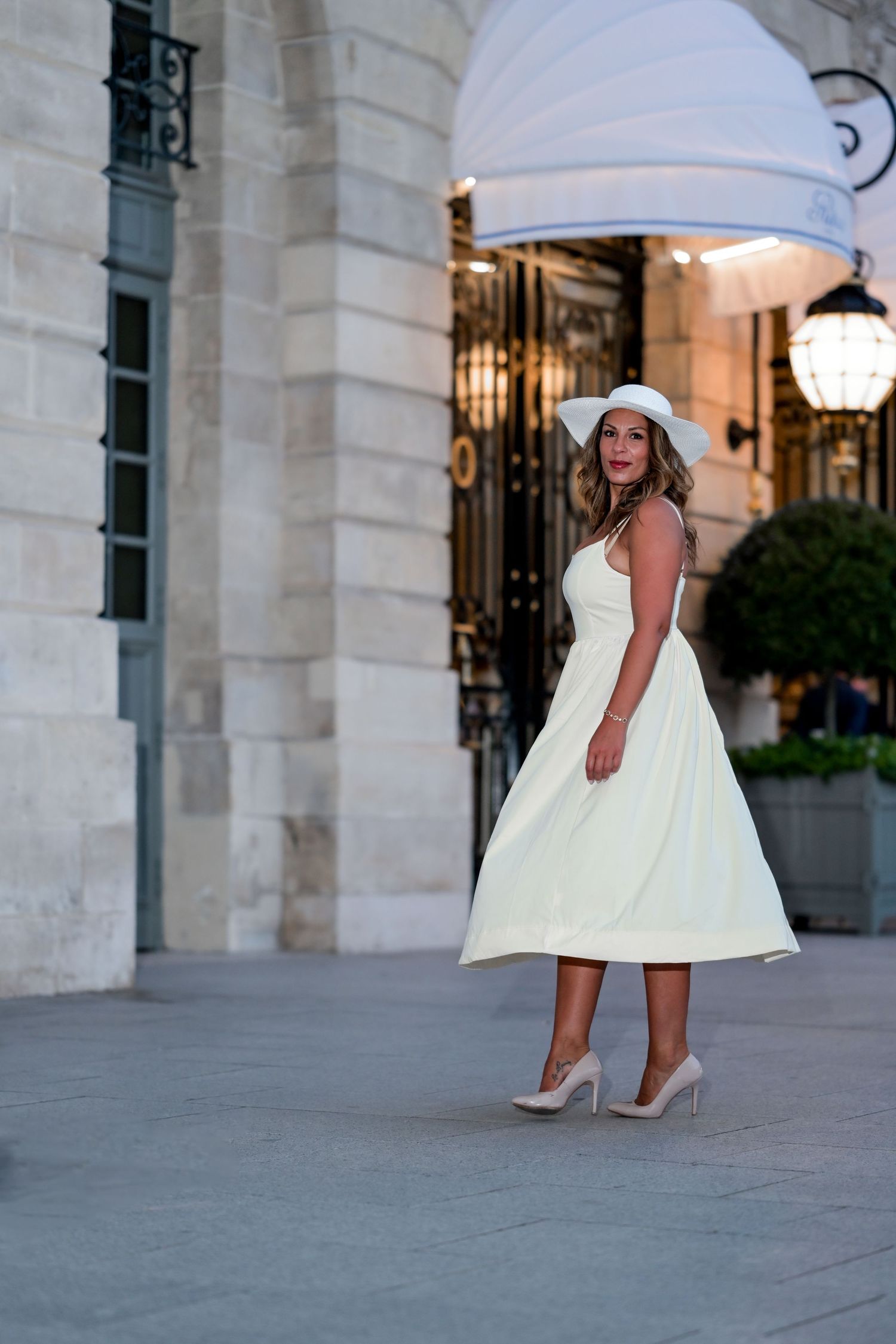 A cream-colored dress and hat ensemble captured against elegant architectural details.