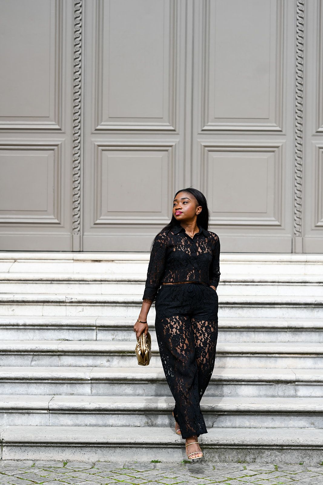 Fashion photo of person in black lace outfit posing on white stone steps.