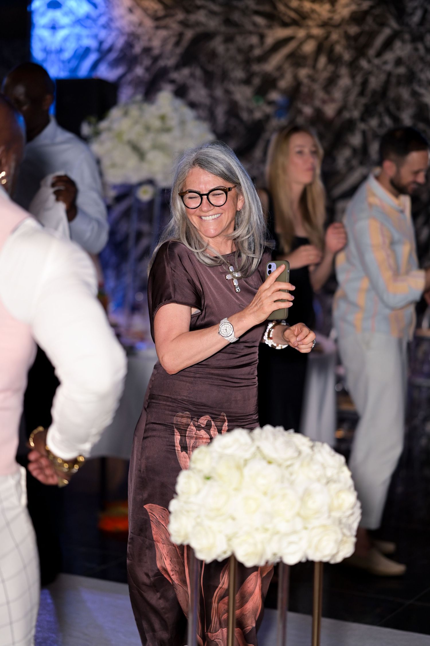 Person in brown dress dancing near white floral arrangements with blue lighting in background.