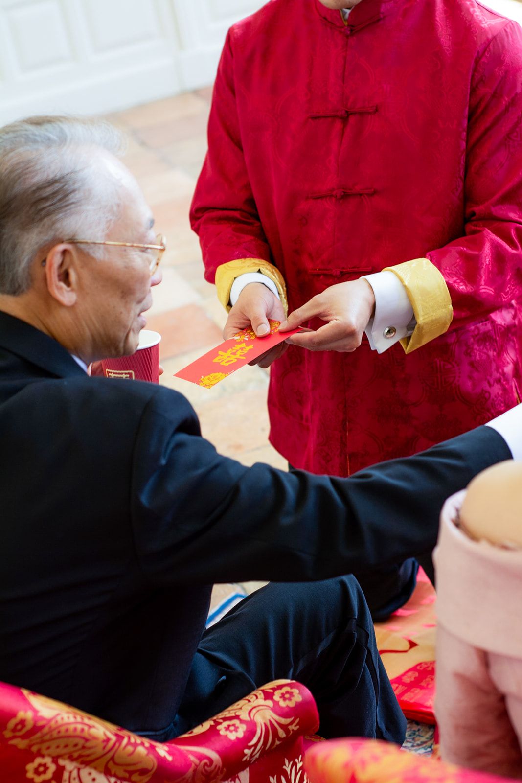 Person in traditional red Chinese attire presenting red envelope during ceremony.
