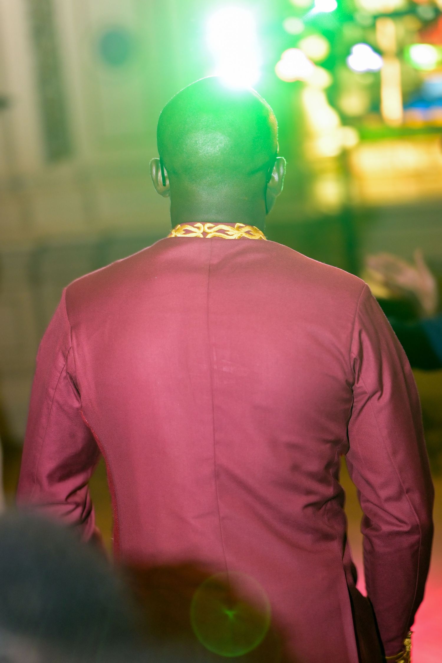 Back view of person in burgundy jacket under green party lights.