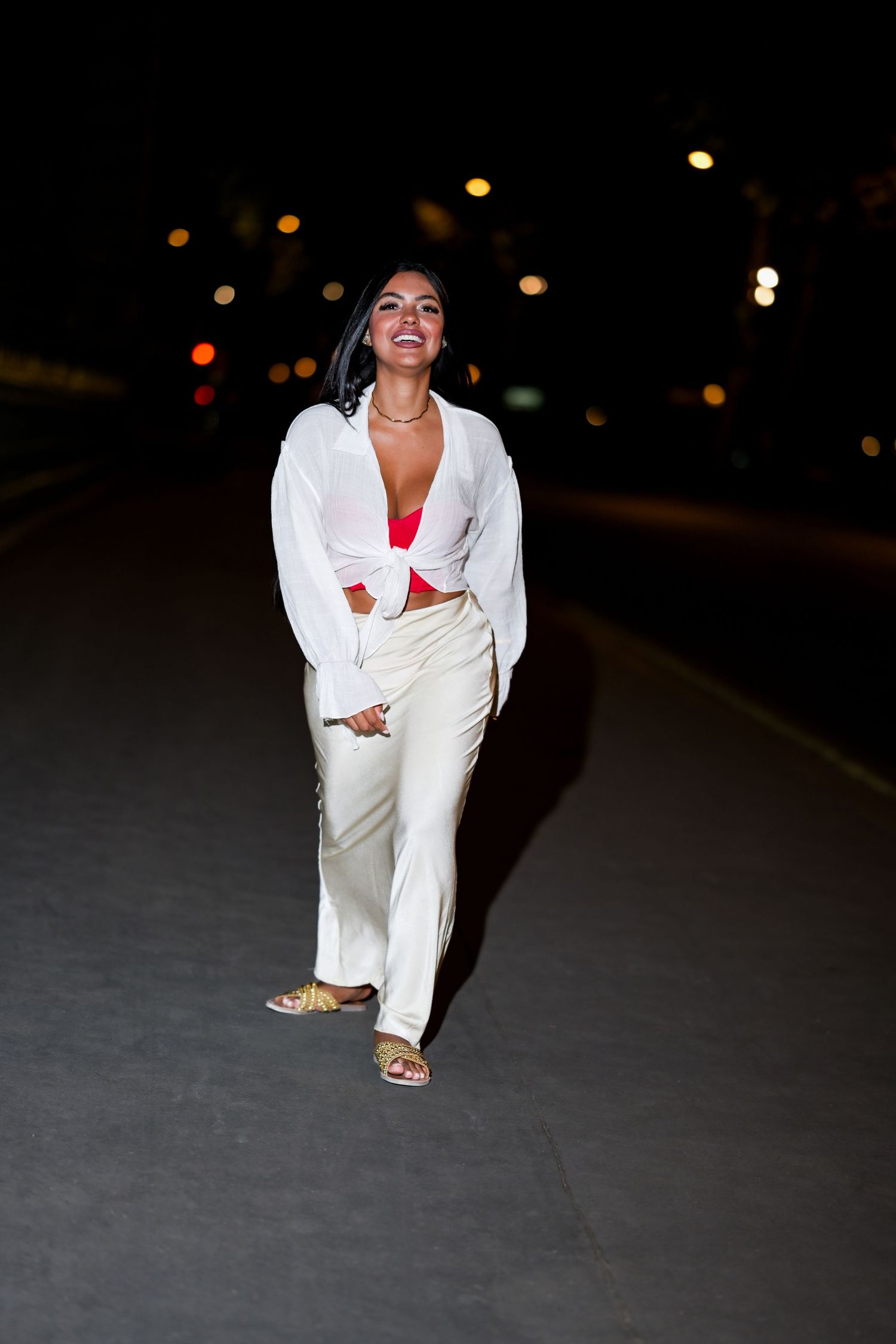 A nighttime street fashion photo featuring a casual white outfit with red accent against city lights.