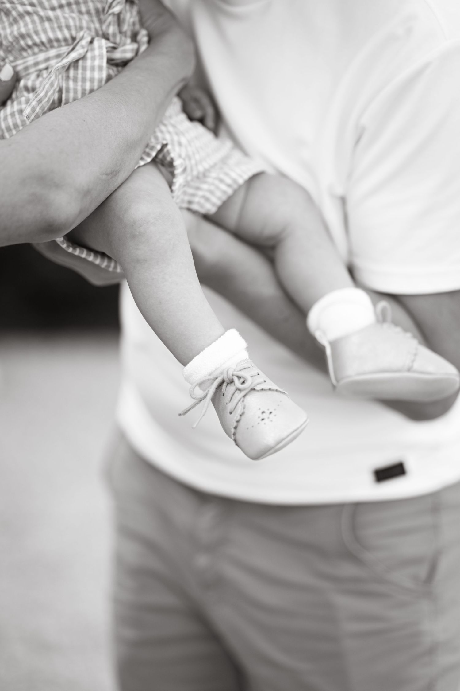 Close-up black and white image of small baby shoes and clothing details.