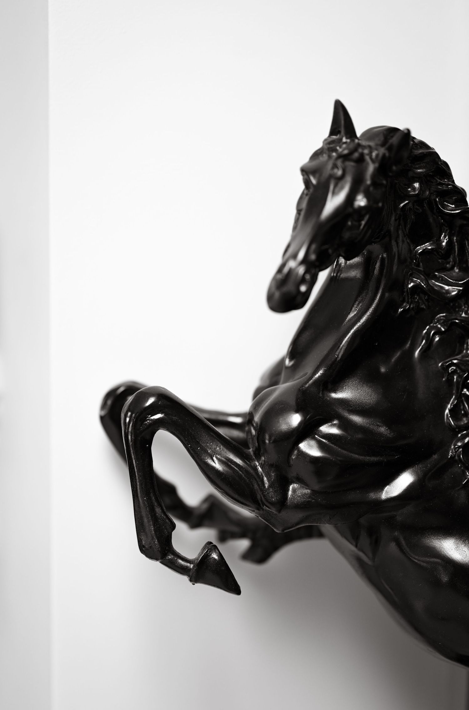 Glossy black sculptural horse figure shown in dramatic side profile against white background.