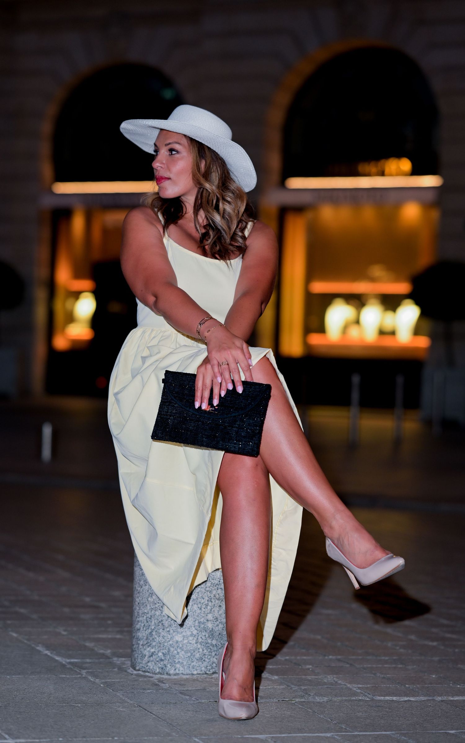 Dramatic pose in white dress and hat against illuminated archways.