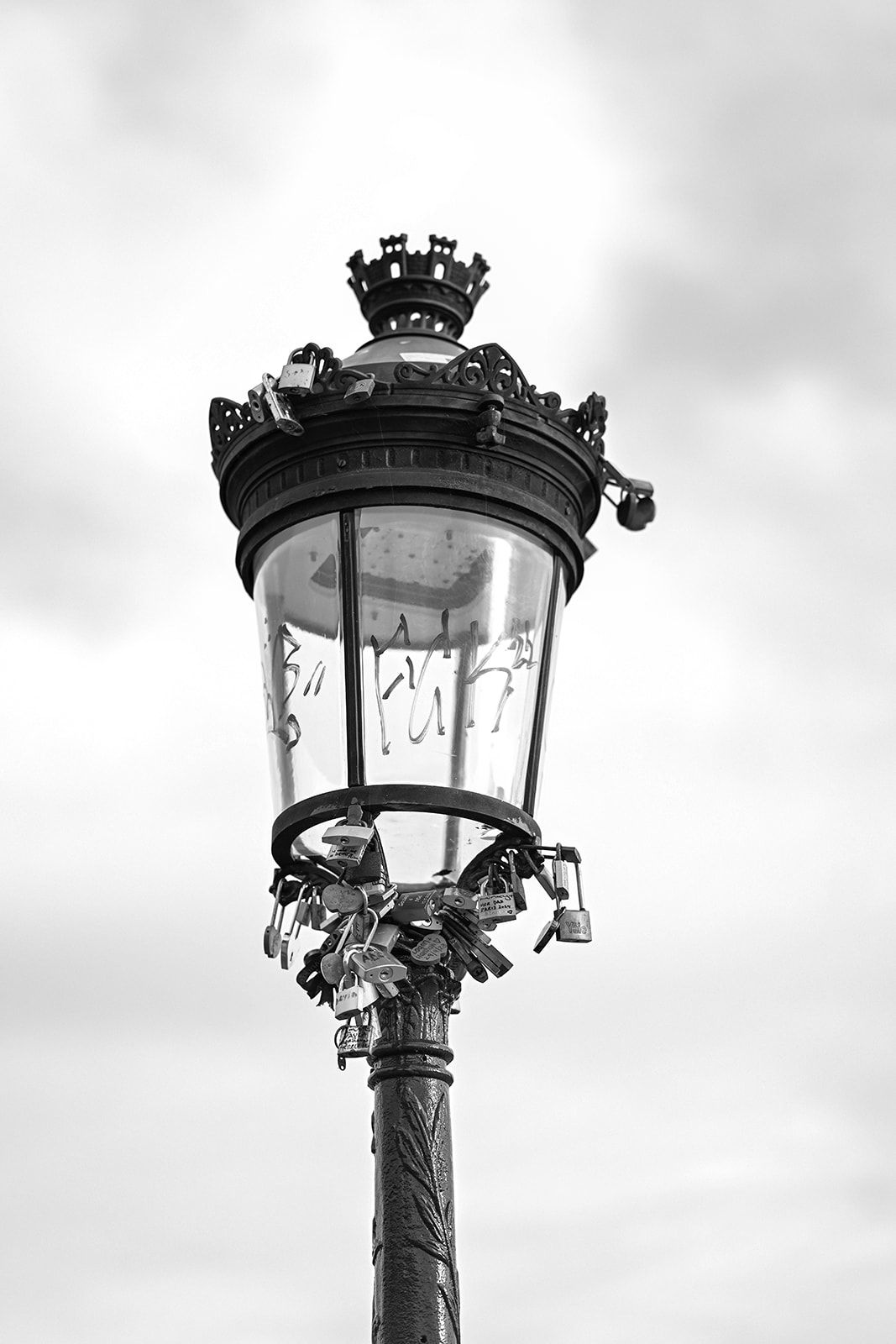 Black and white vintage street lamp with ornate crown detail against cloudy sky.