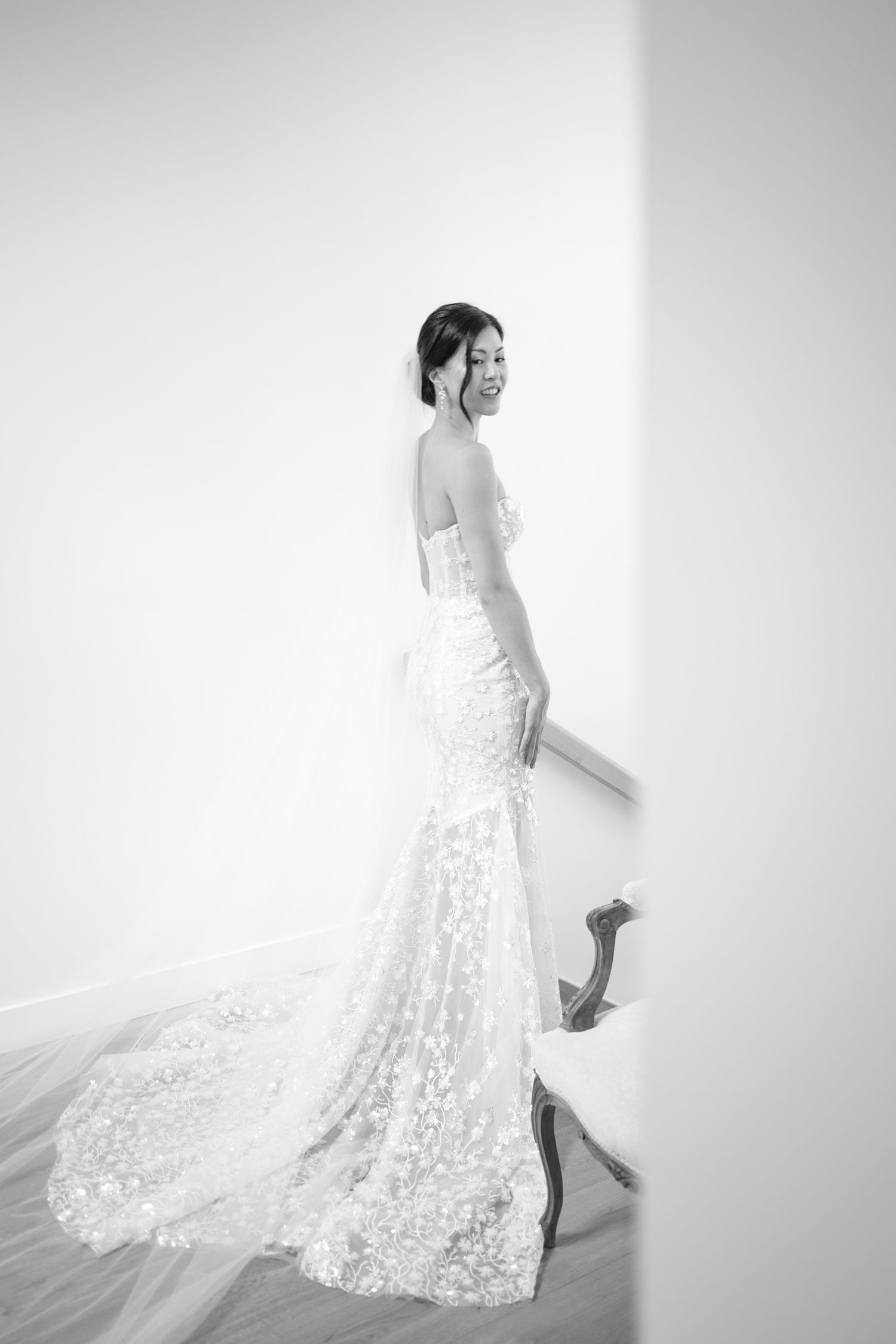 Bride in strapless lace mermaid wedding gown with floral appliques and long train, posing elegantly in black and white photo.