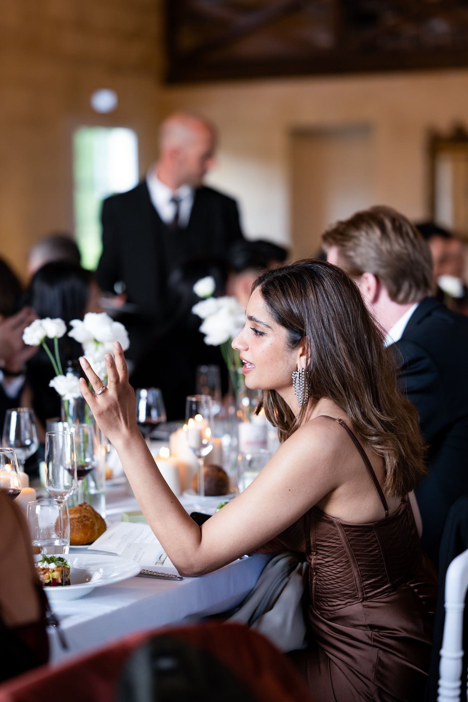 Guest in brown dress dining at formal event with white table settings.