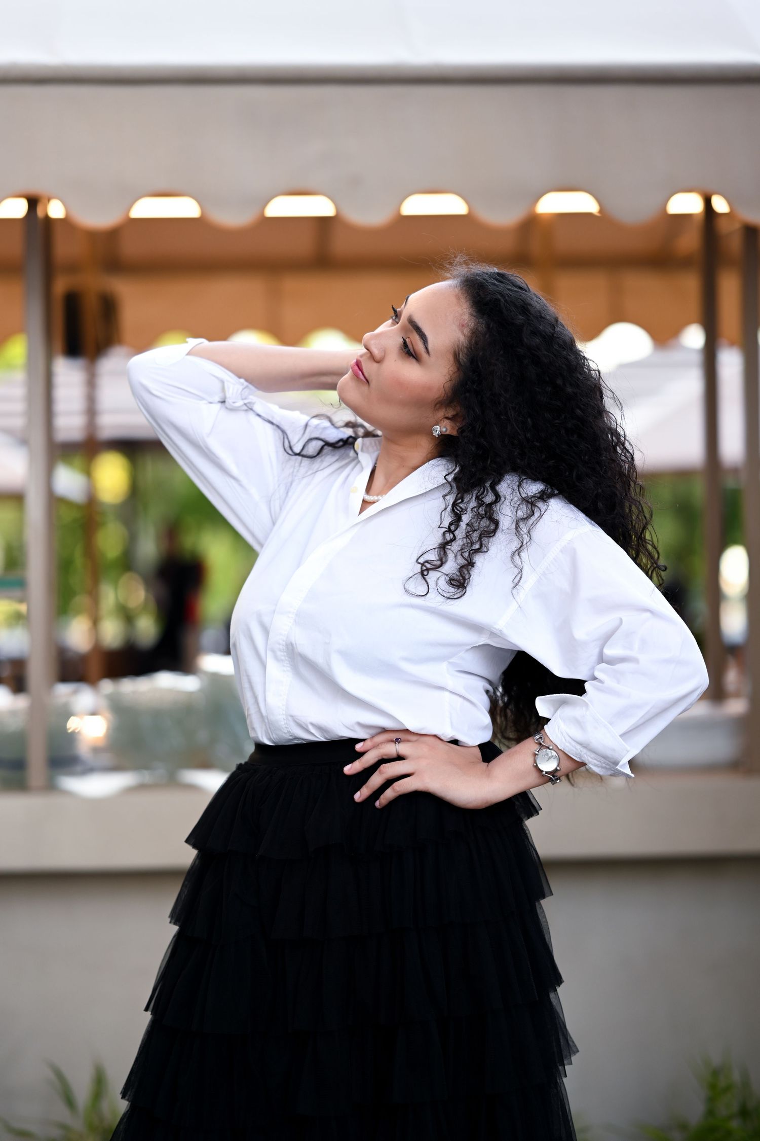 Dancer in white shirt and black tulle skirt performs expressive poses in outdoor setting.