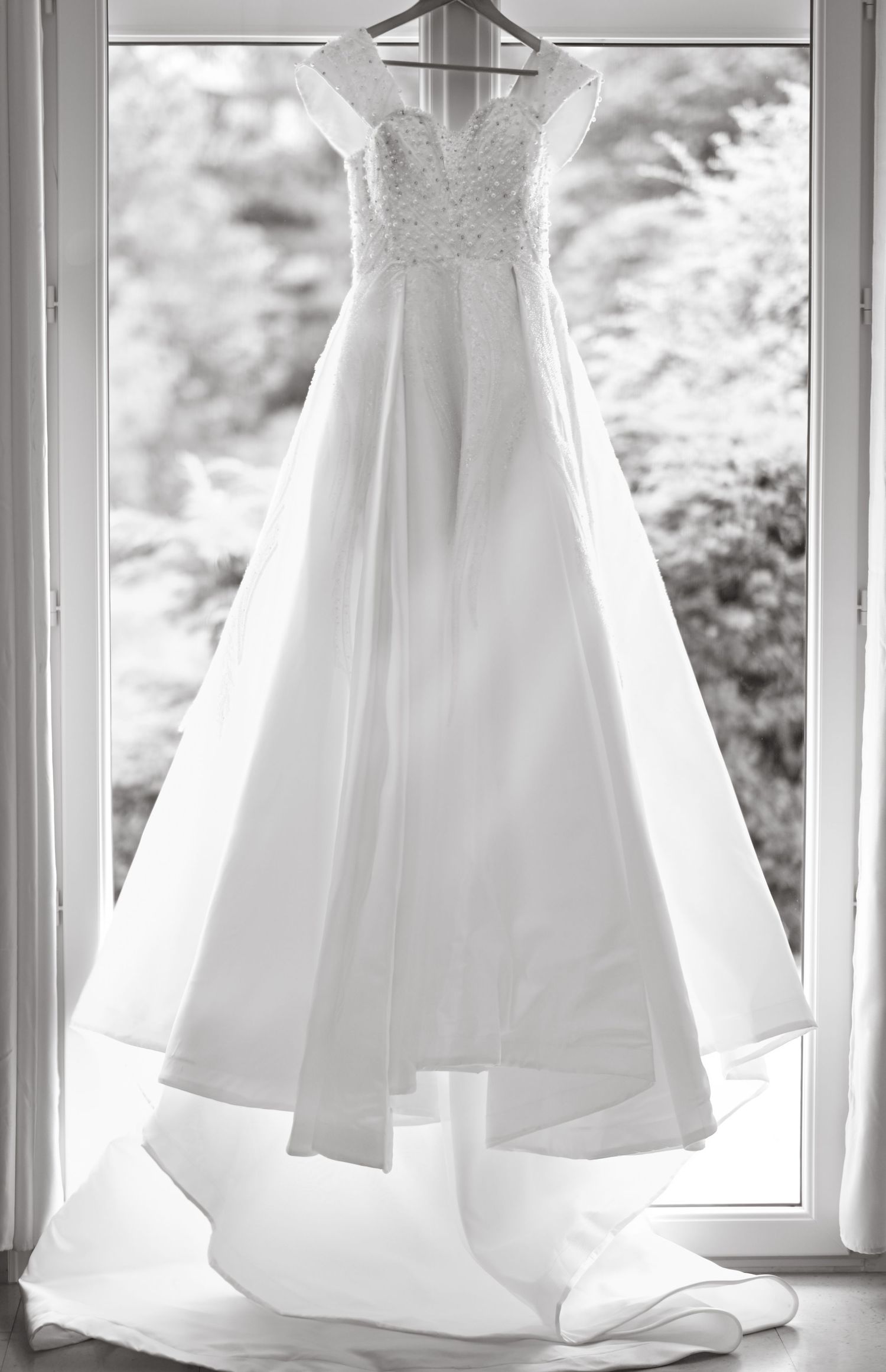 White wedding dresses hanging in a row by a window creating an elegant display.