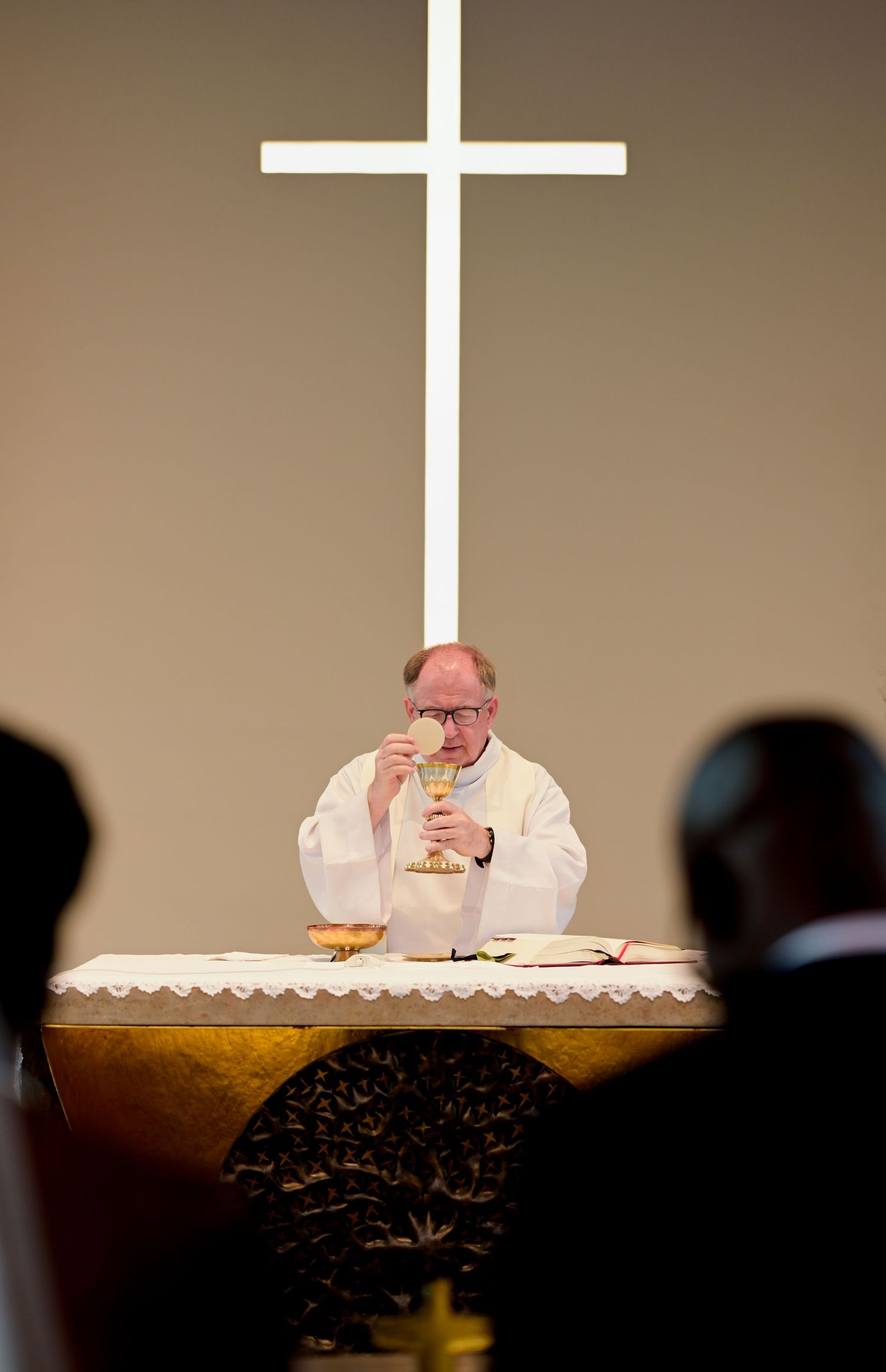 Priest conducting communion service at altar with white cross in background.