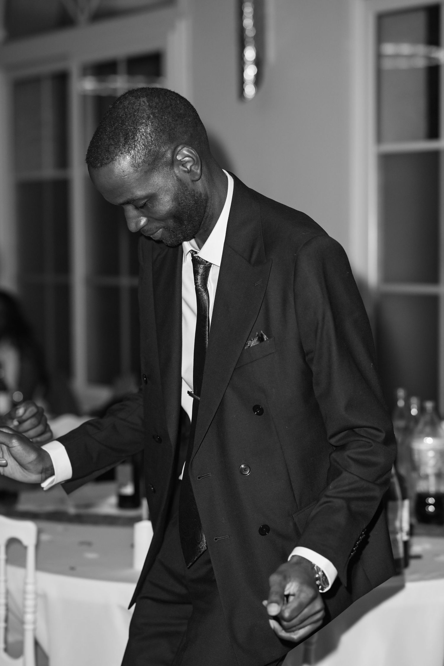 A candid black and white photo of a person in a suit smiling and looking down.