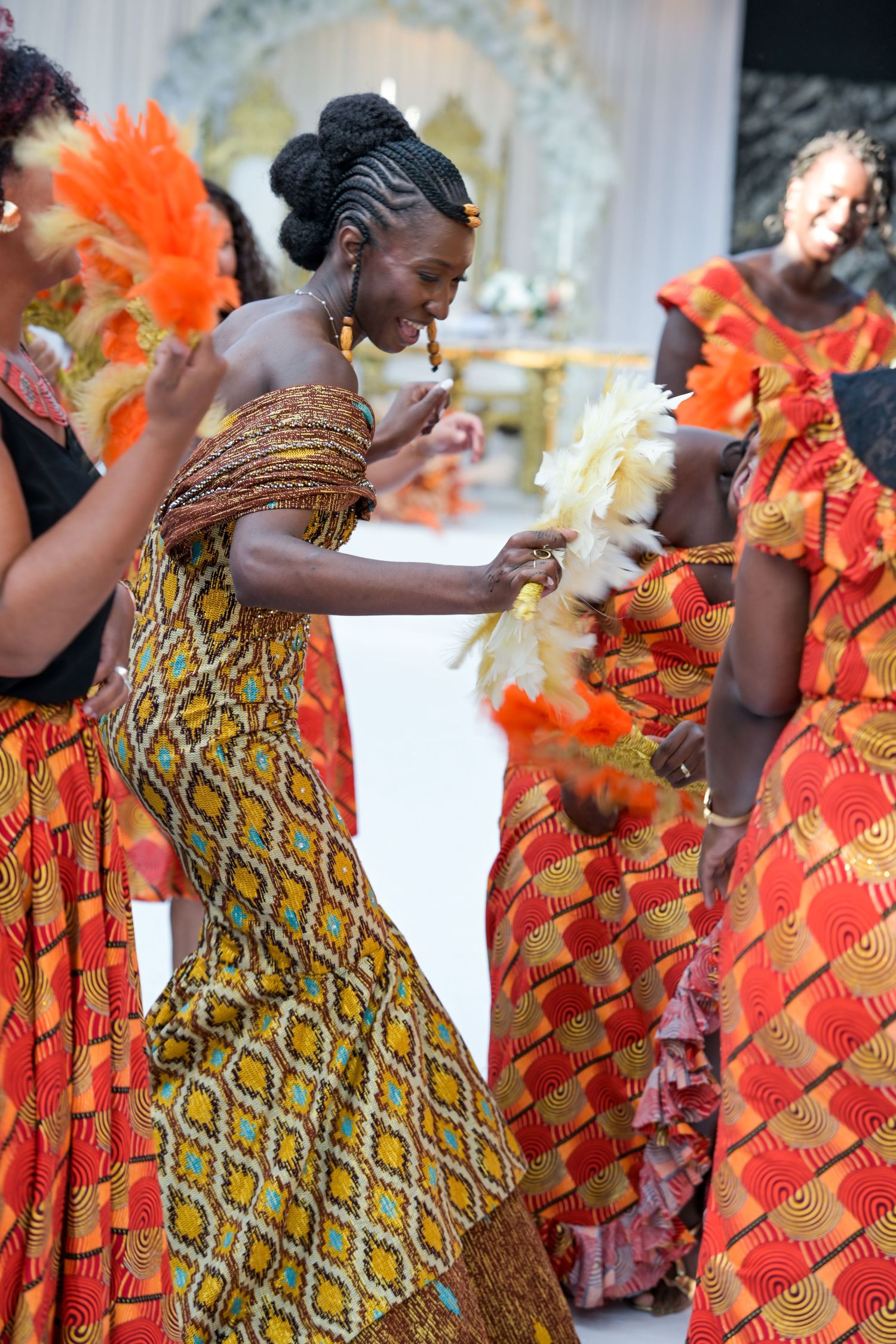 Women wearing colorful African wax print dresses in orange and yellow patterns at a festive gathering.