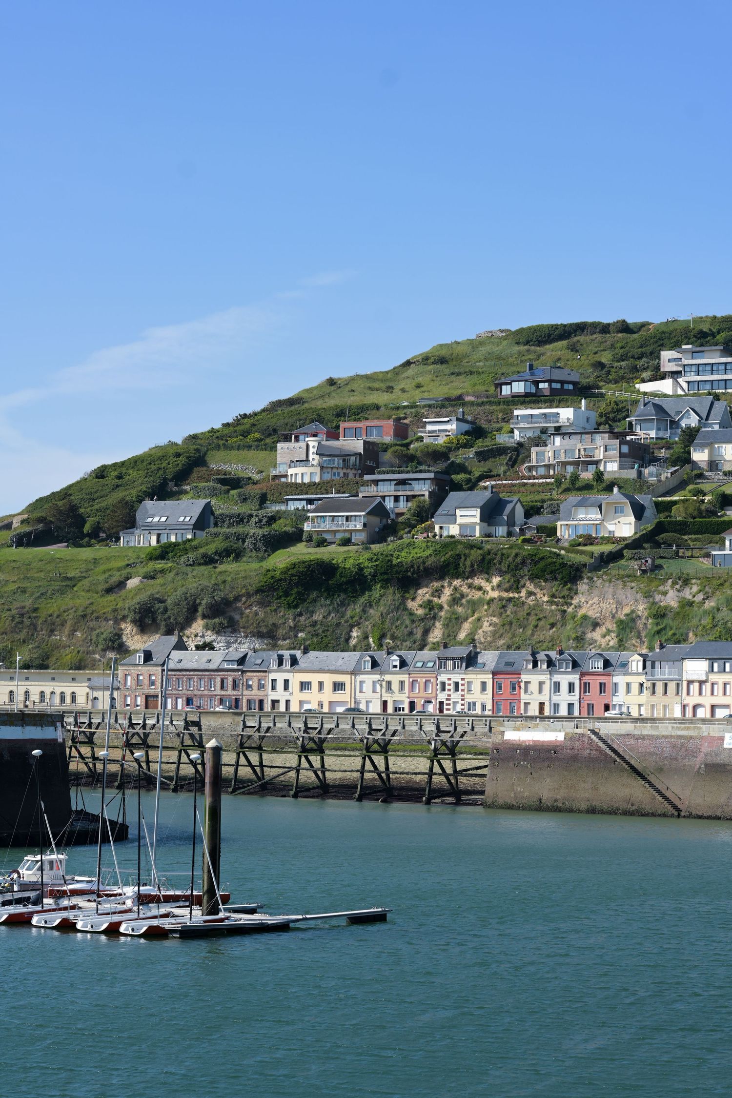 Colorful coastal houses line a hillside above a marina in a seaside town.