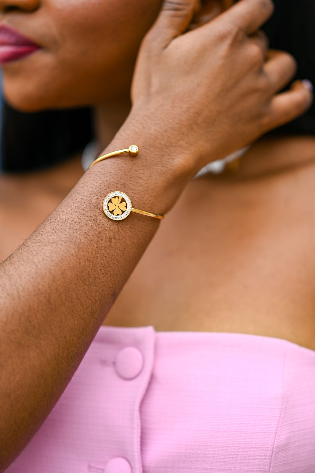 Gold bangle bracelet with circular charm detail shown on wrist against pink dress.