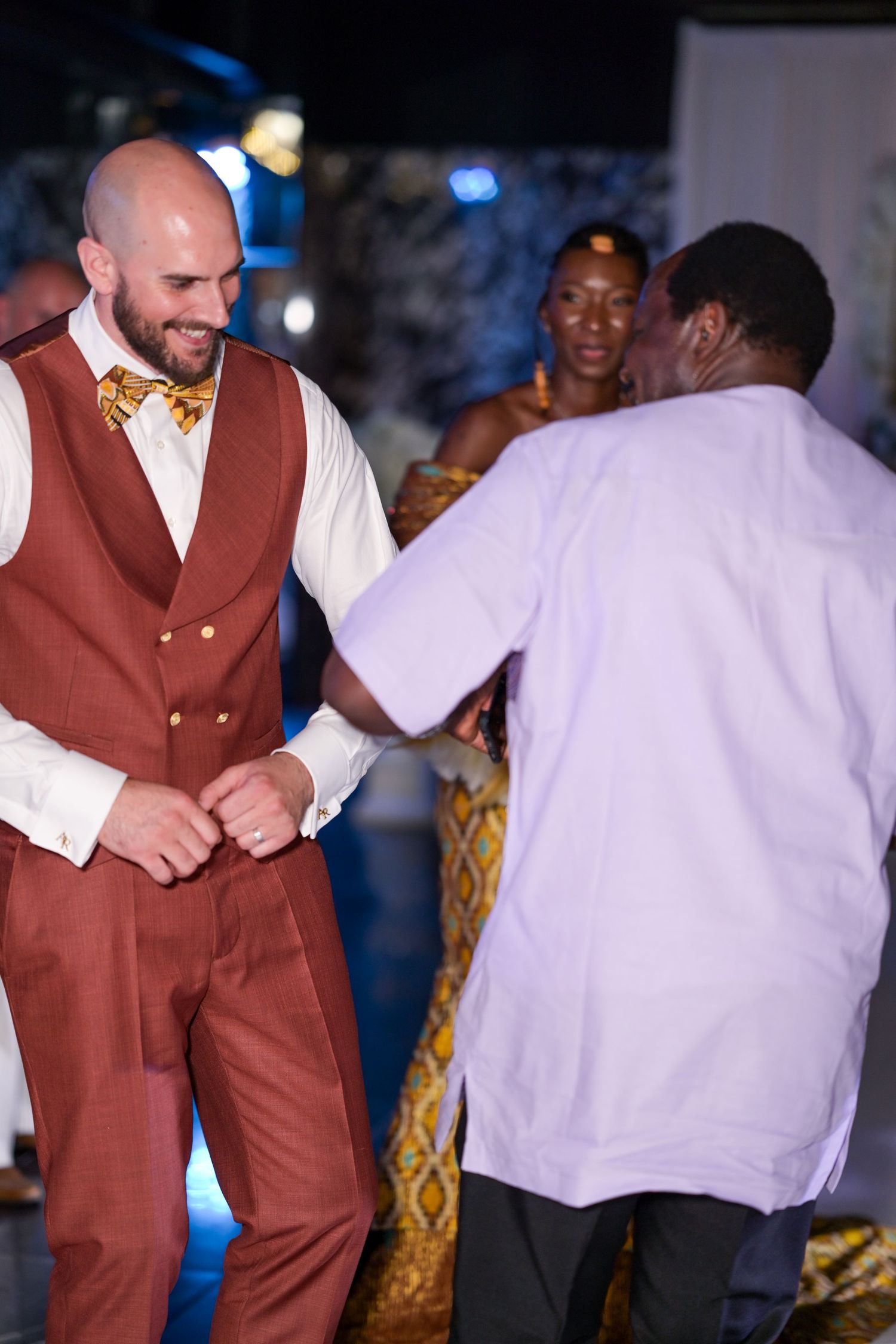 People dancing at a party, with someone wearing a brown suit visible in the frame.