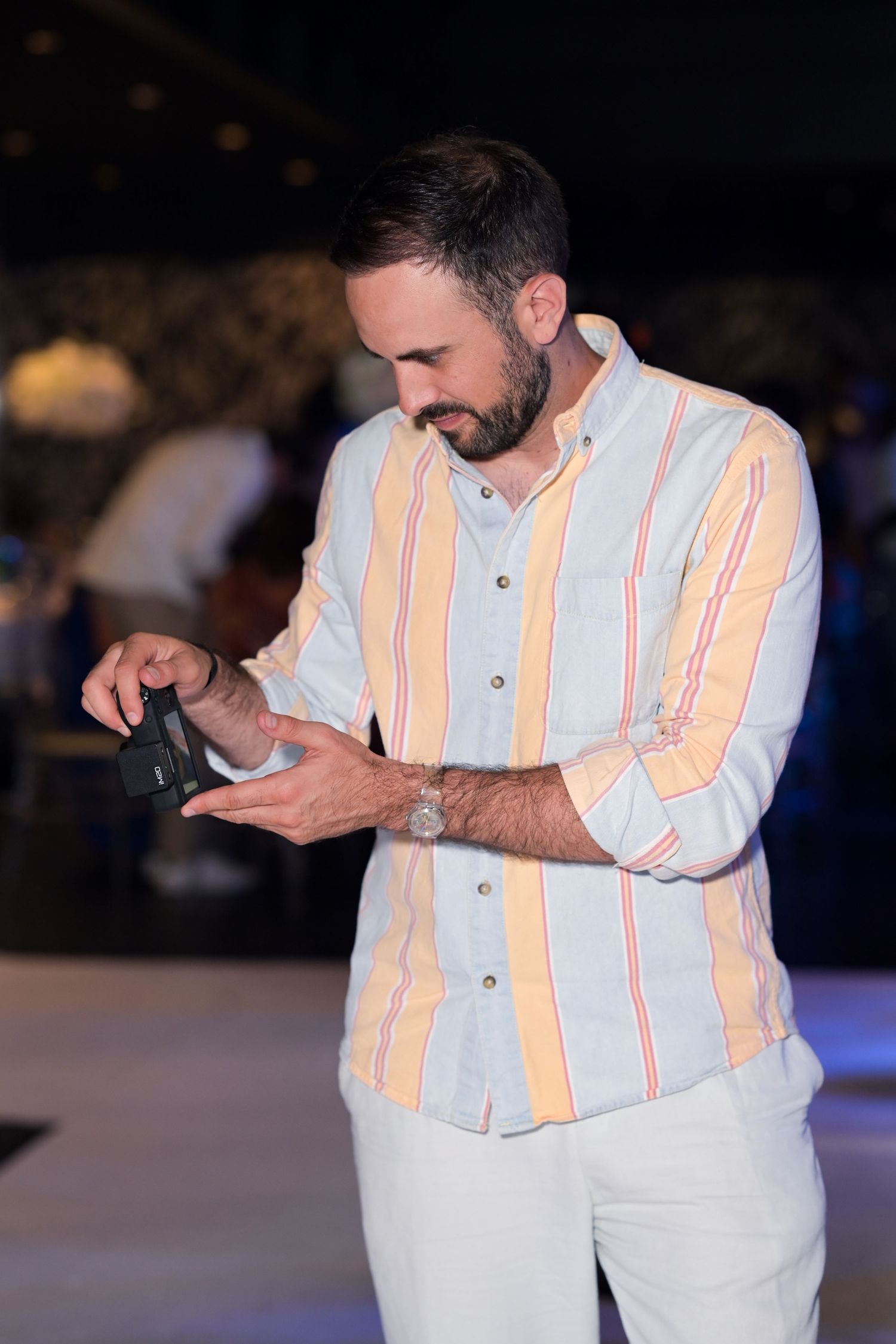 Man in striped white and peach shirt looking down at something in his hands.