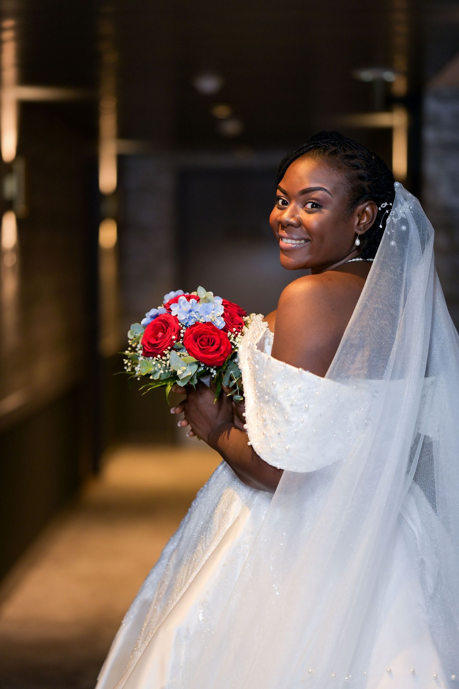 Joyful bride holds red and white bouquet while wearing an off-shoulder wedding gown.