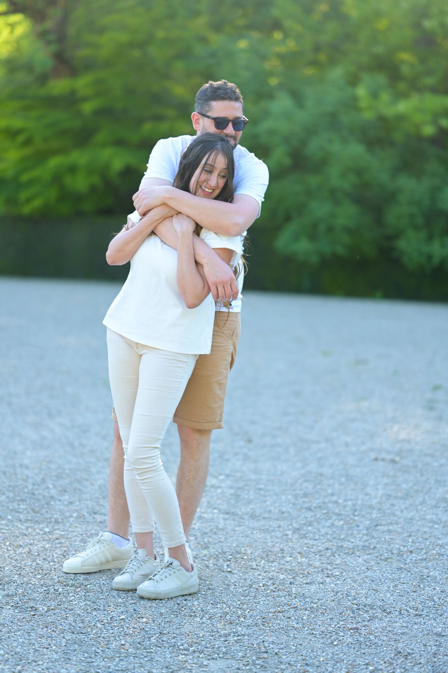 Sweet embraces captured in casual outdoor photoshoot on gravel surface.