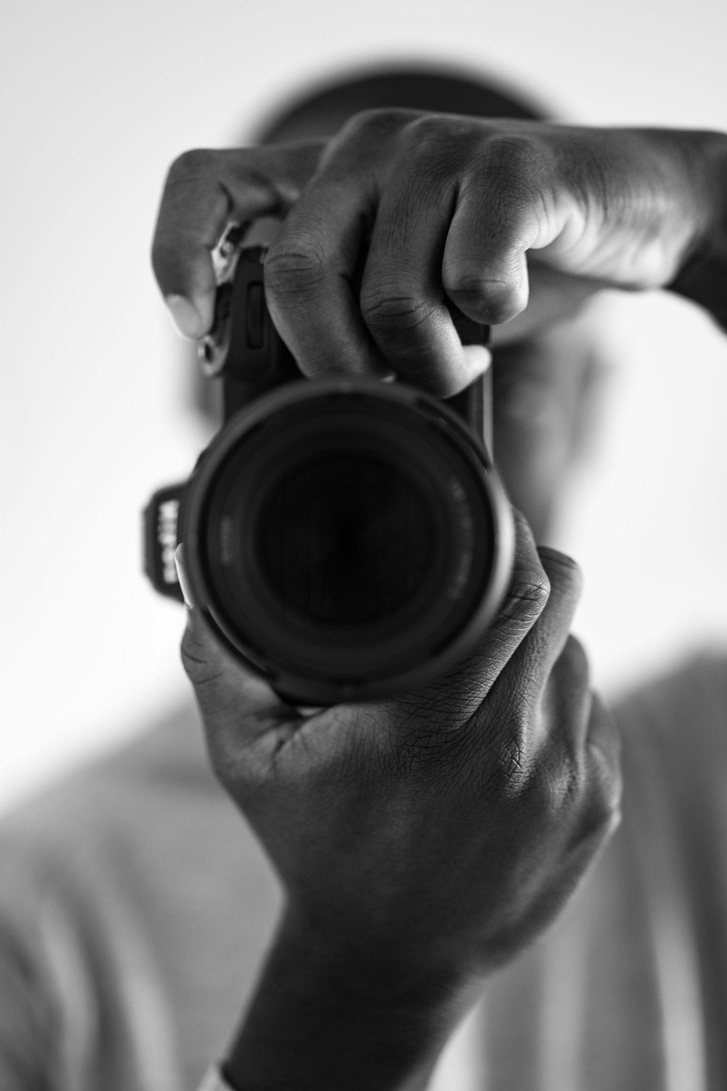 Close-up black and white shot of hands holding a camera lens in focus position.