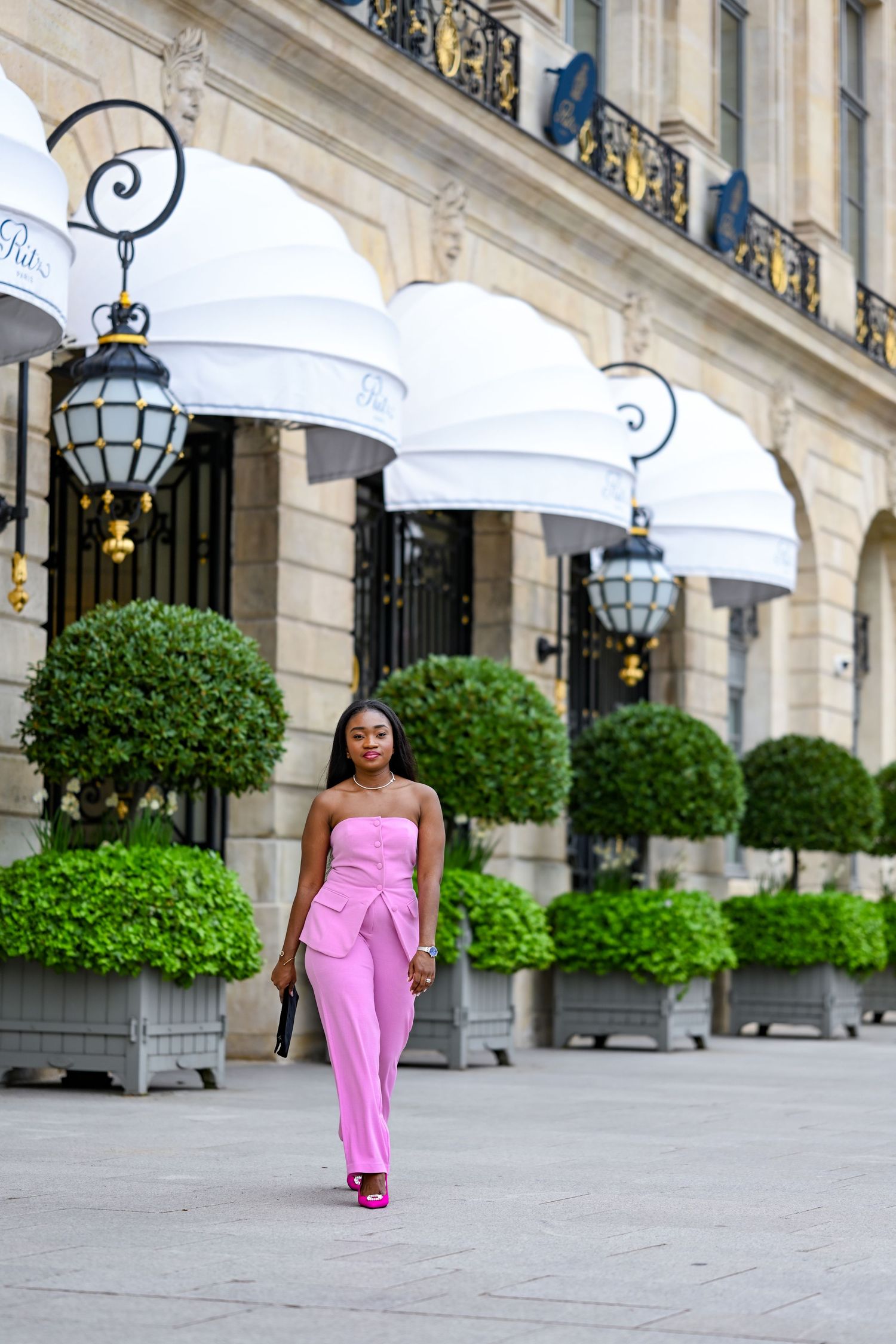 Pink strapless jumpsuit styled against elegant building facade with white awnings.