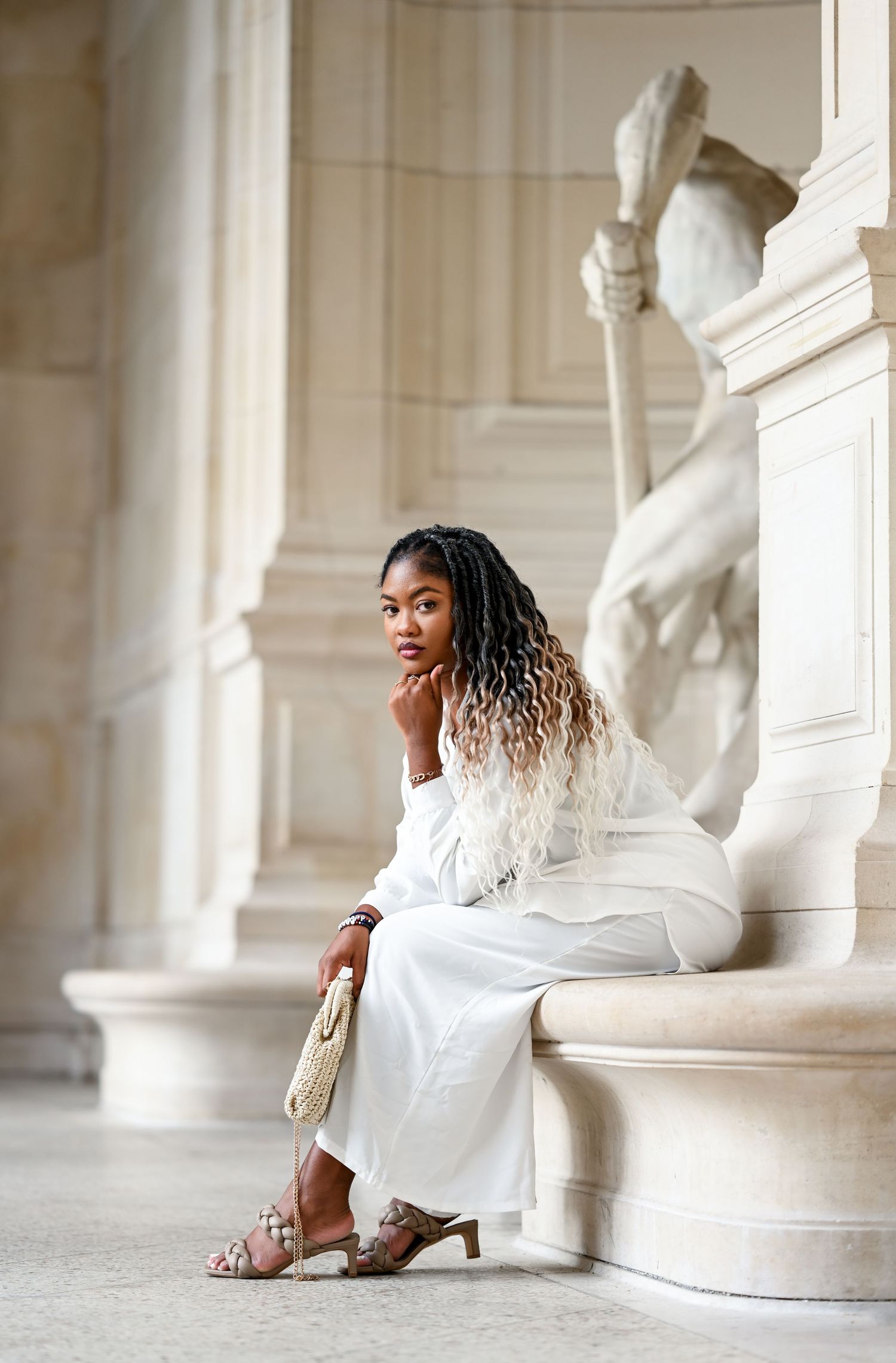 Fashion portrait in minimalist white outfit against architectural backdrop with classical statue.