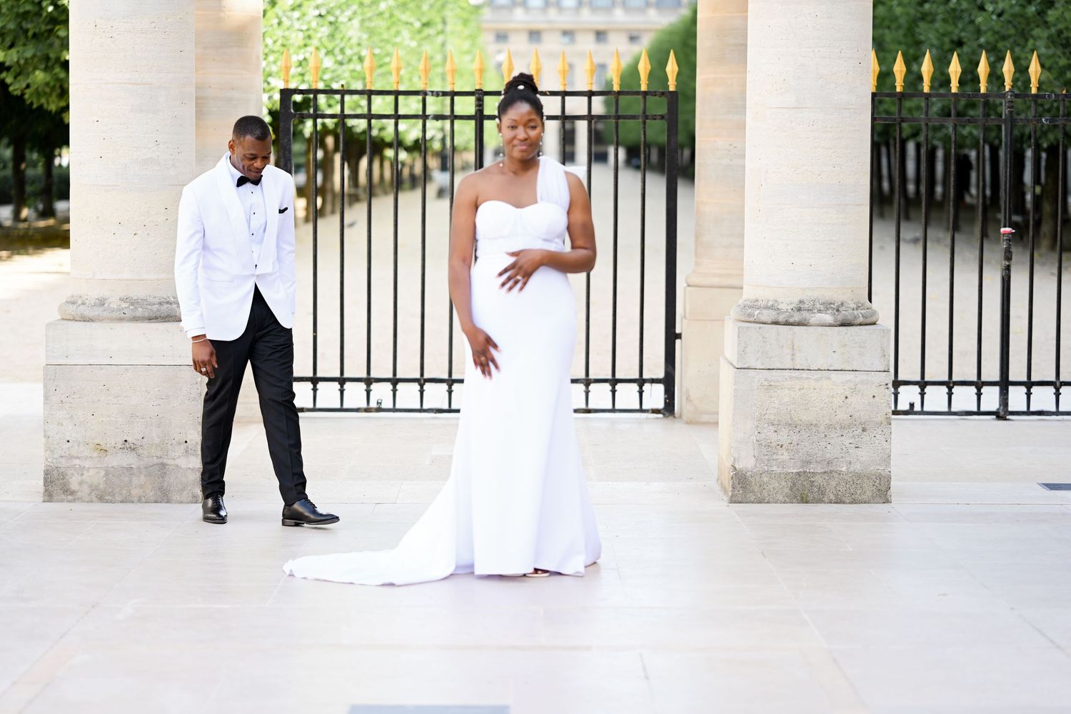 Wedding couple posing separately in elegant white attire by ornate gate.