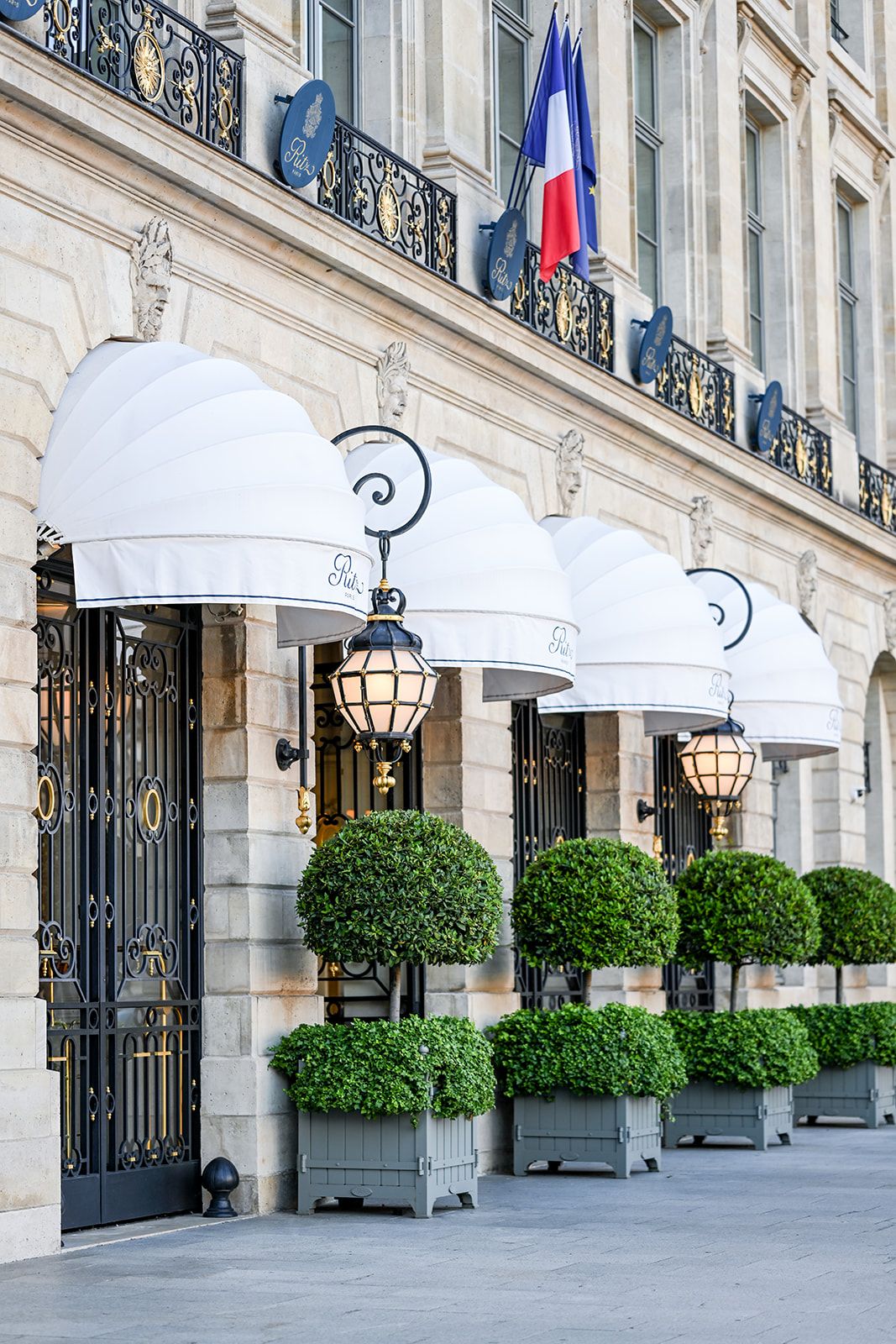 Elegant Parisian building facade with white awnings, lanterns and manicured topiaries.