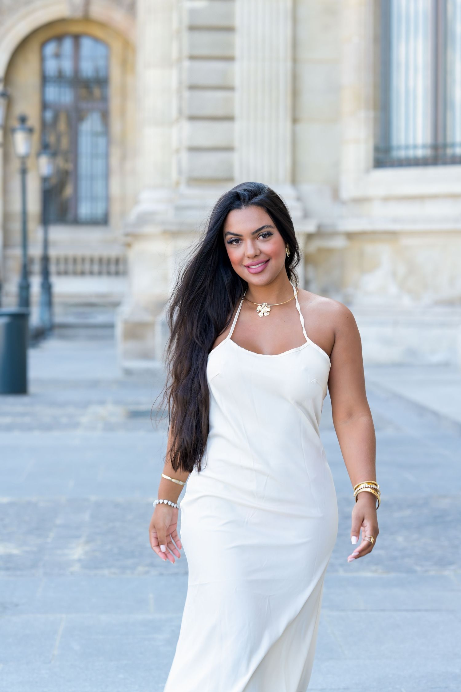 A person in an elegant white dress stands confidently against a historic building backdrop.