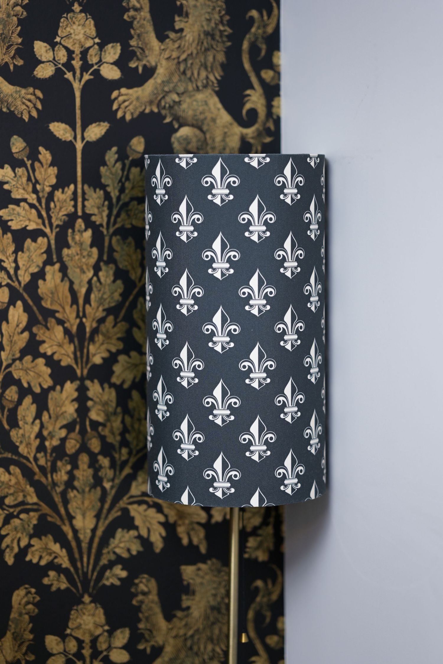 A black and gray fleur-de-lis patterned lampshade against a gold damask wallpaper.