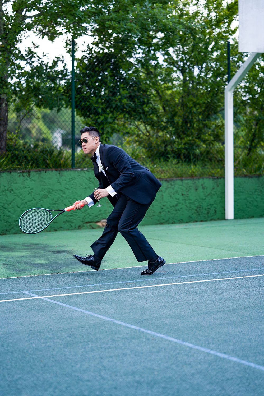 Businessman in suit diving dramatically on outdoor tennis court.