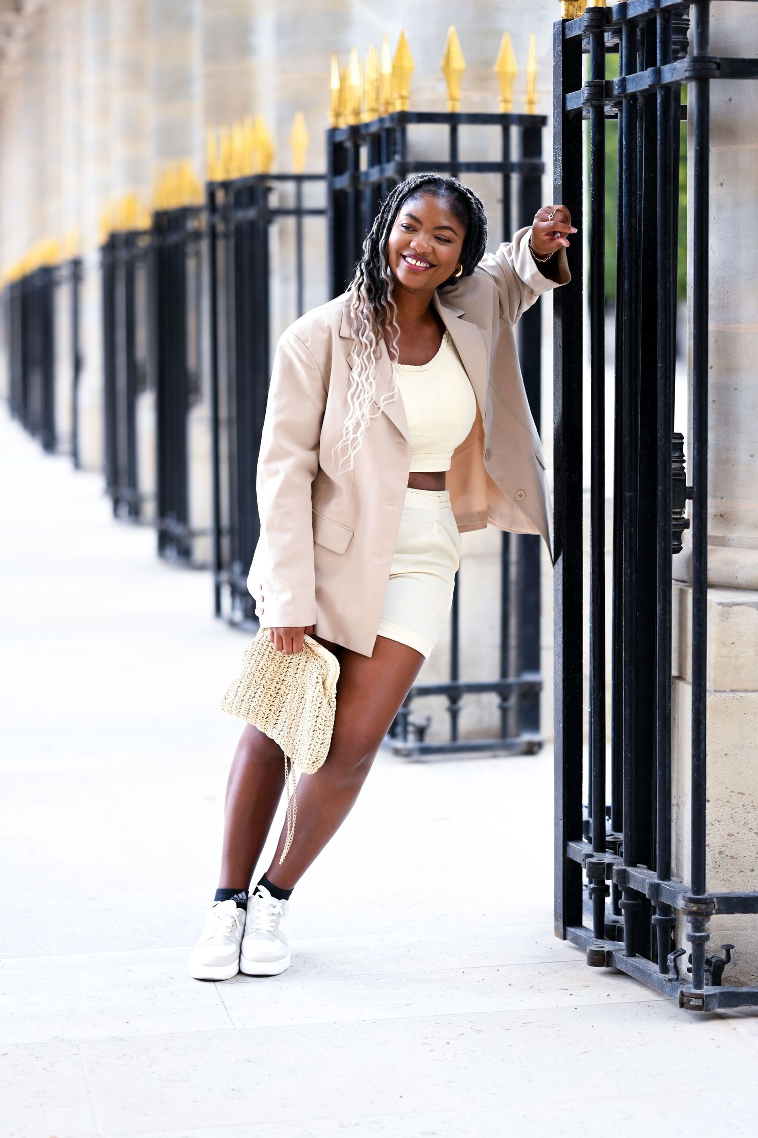 Fashion model poses in cream colored blazer and white outfit against ornate architectural backdrop.