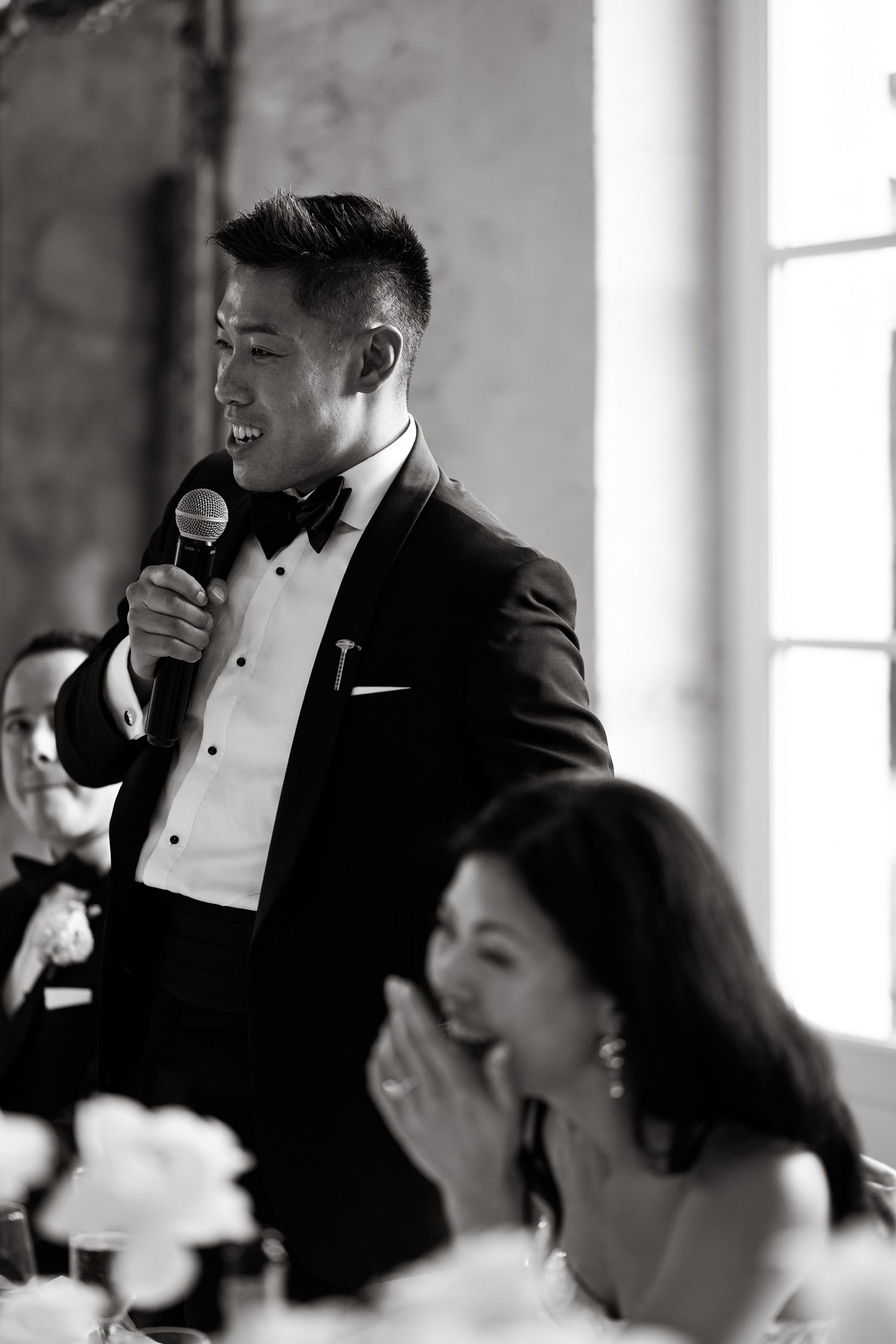 Speaker delivers toast at formal dinner event while guests react with laughter.