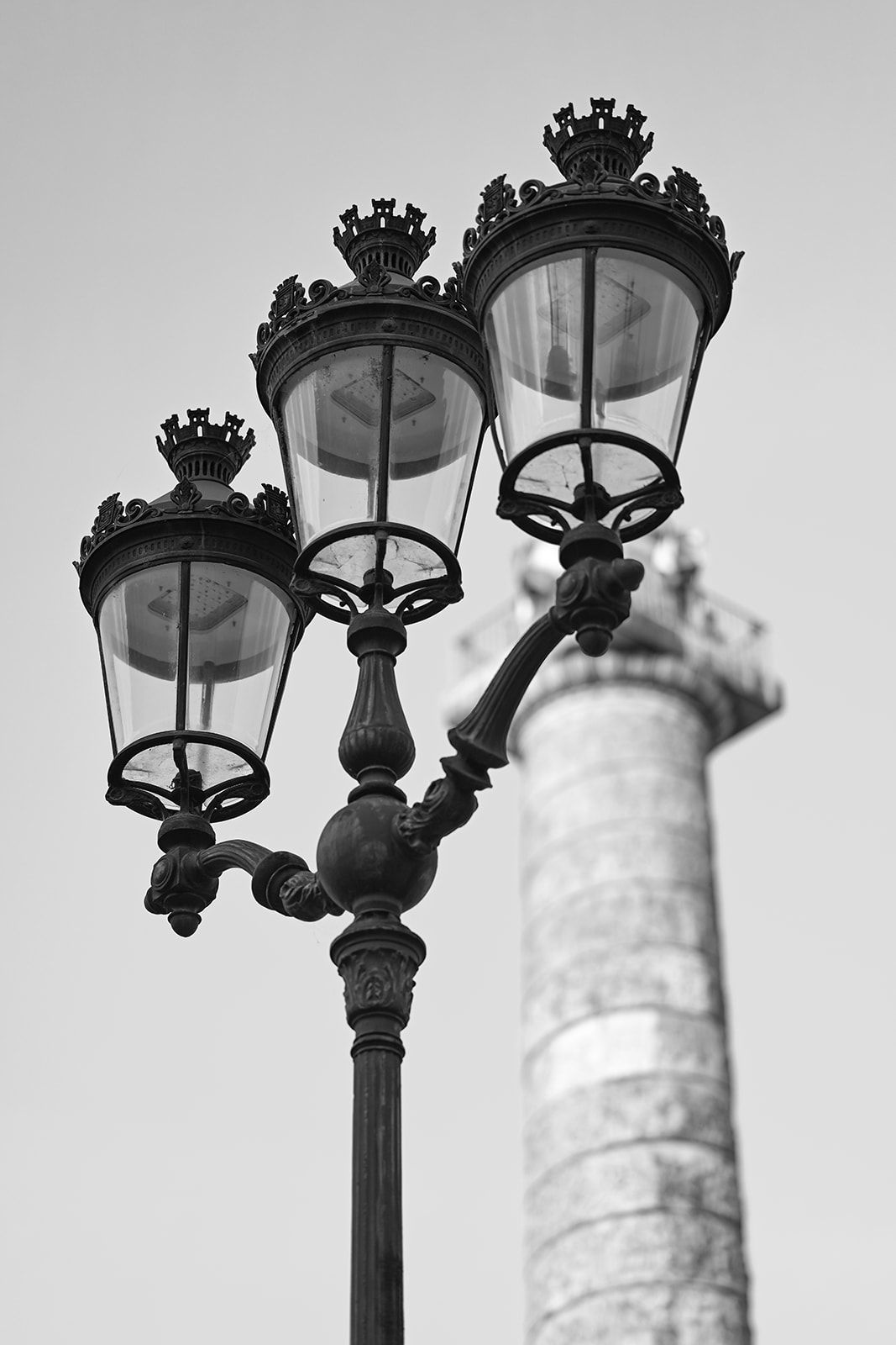 Ornate vintage street lamp with three black iron lanterns against a blurred column background.