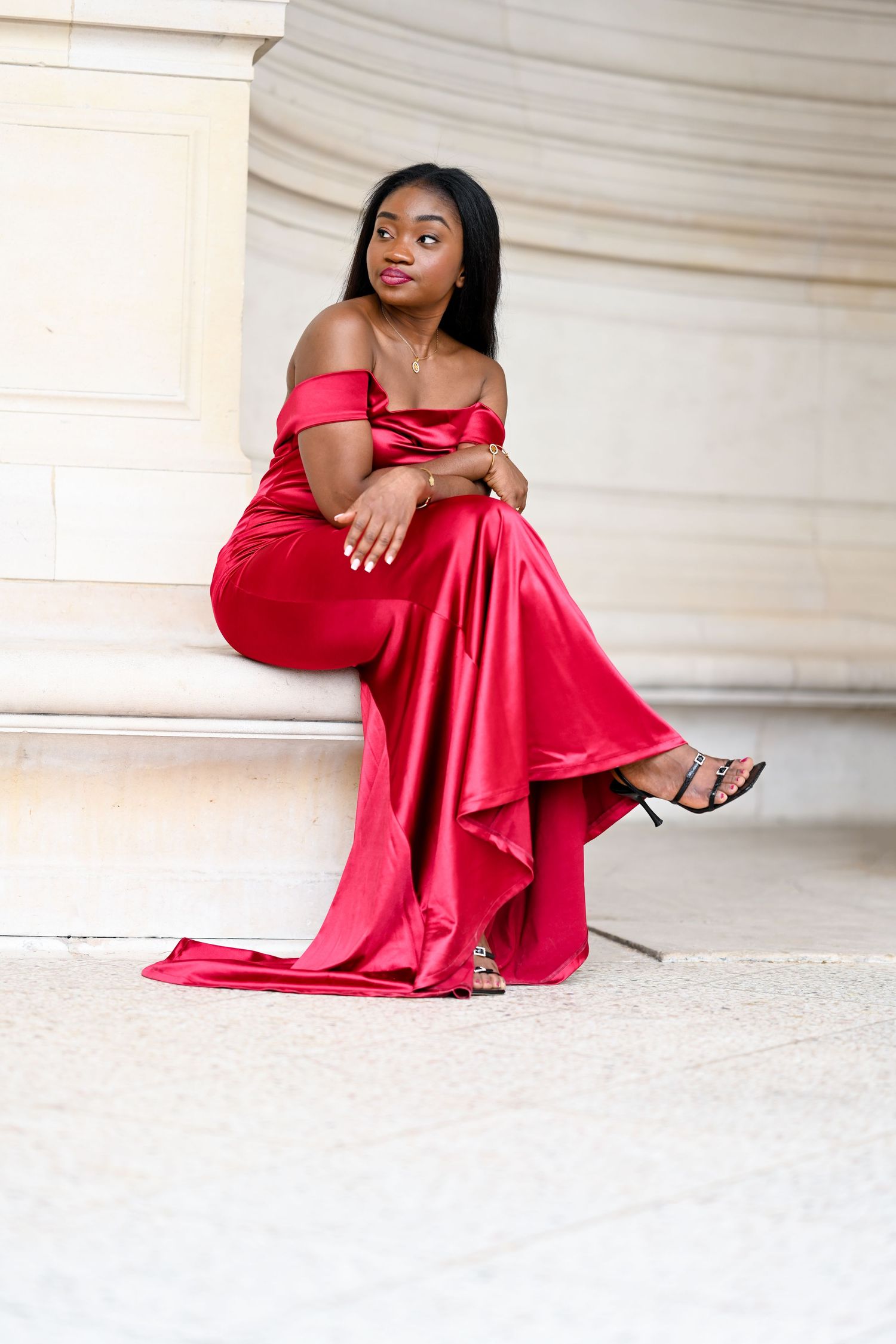 Elegant red off-shoulder gown styled with delicate jewelry against marble backdrop.