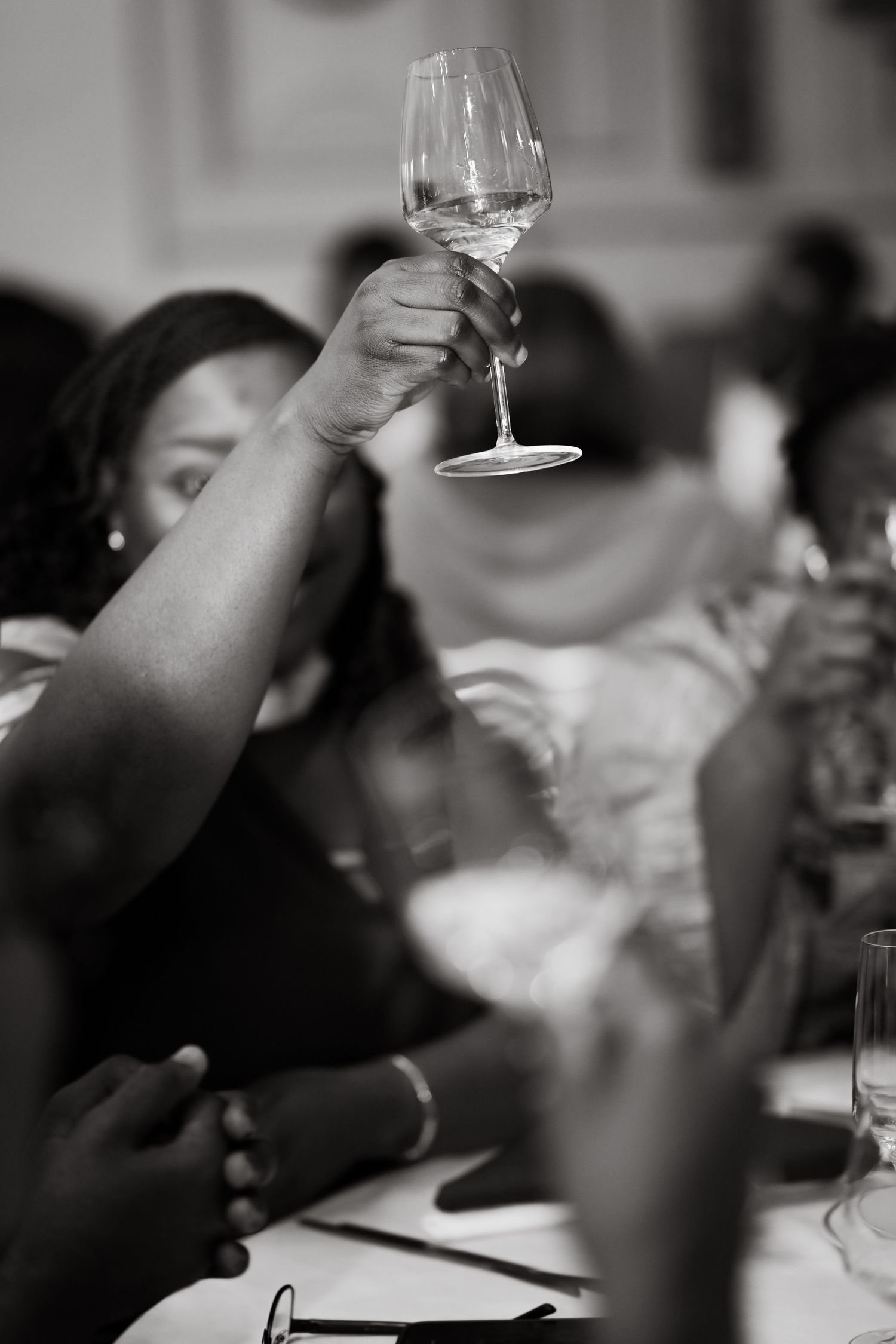 A wine glass being held up during a celebratory toast at a formal dinner gathering.