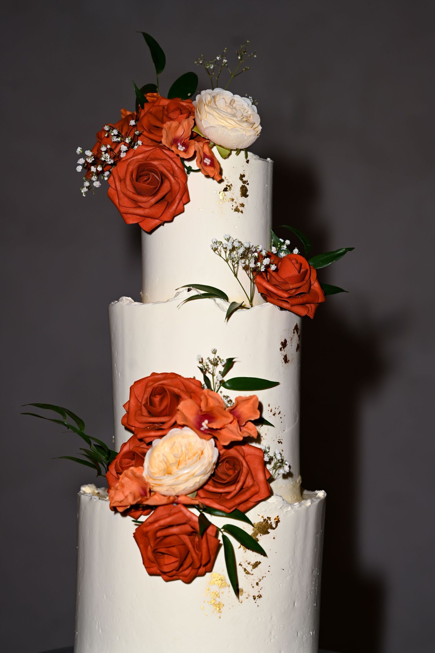 Three-tiered white wedding cake adorned with coral roses and baby's breath.