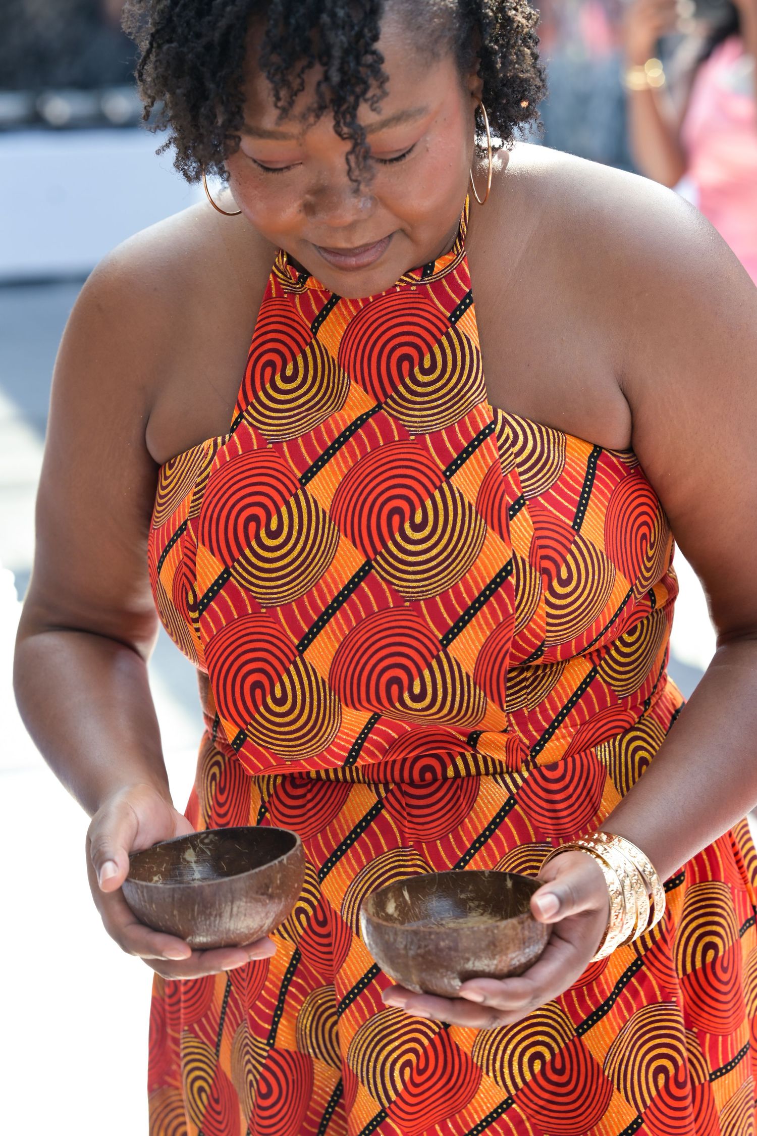 Woman in vibrant orange and black spiral patterned dress holding a bowl.