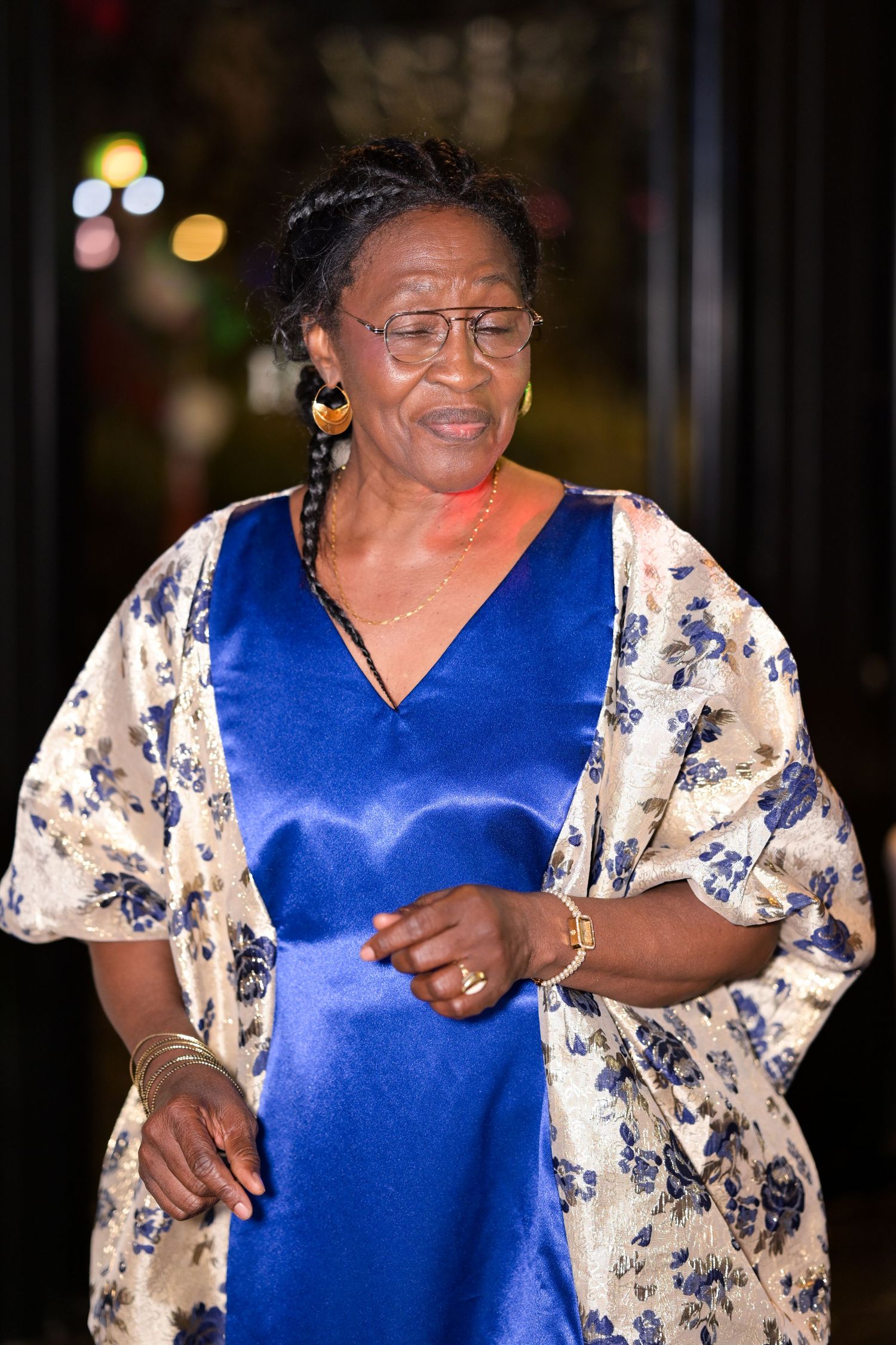 Woman in blue and white floral dress smiling and dancing at evening celebration.