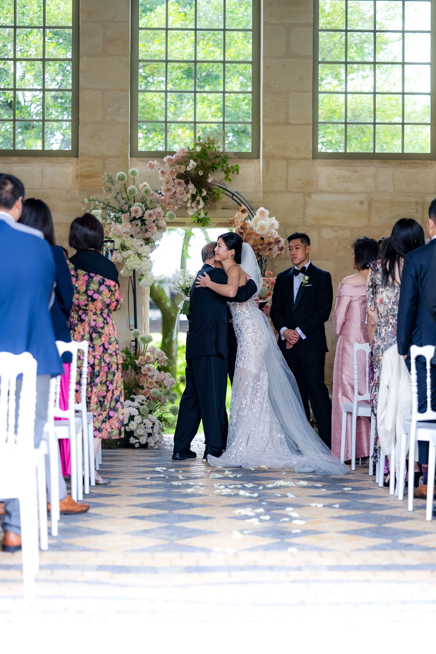 Wedding ceremony in progress under a beautiful floral arch with guests seated in white chairs.
