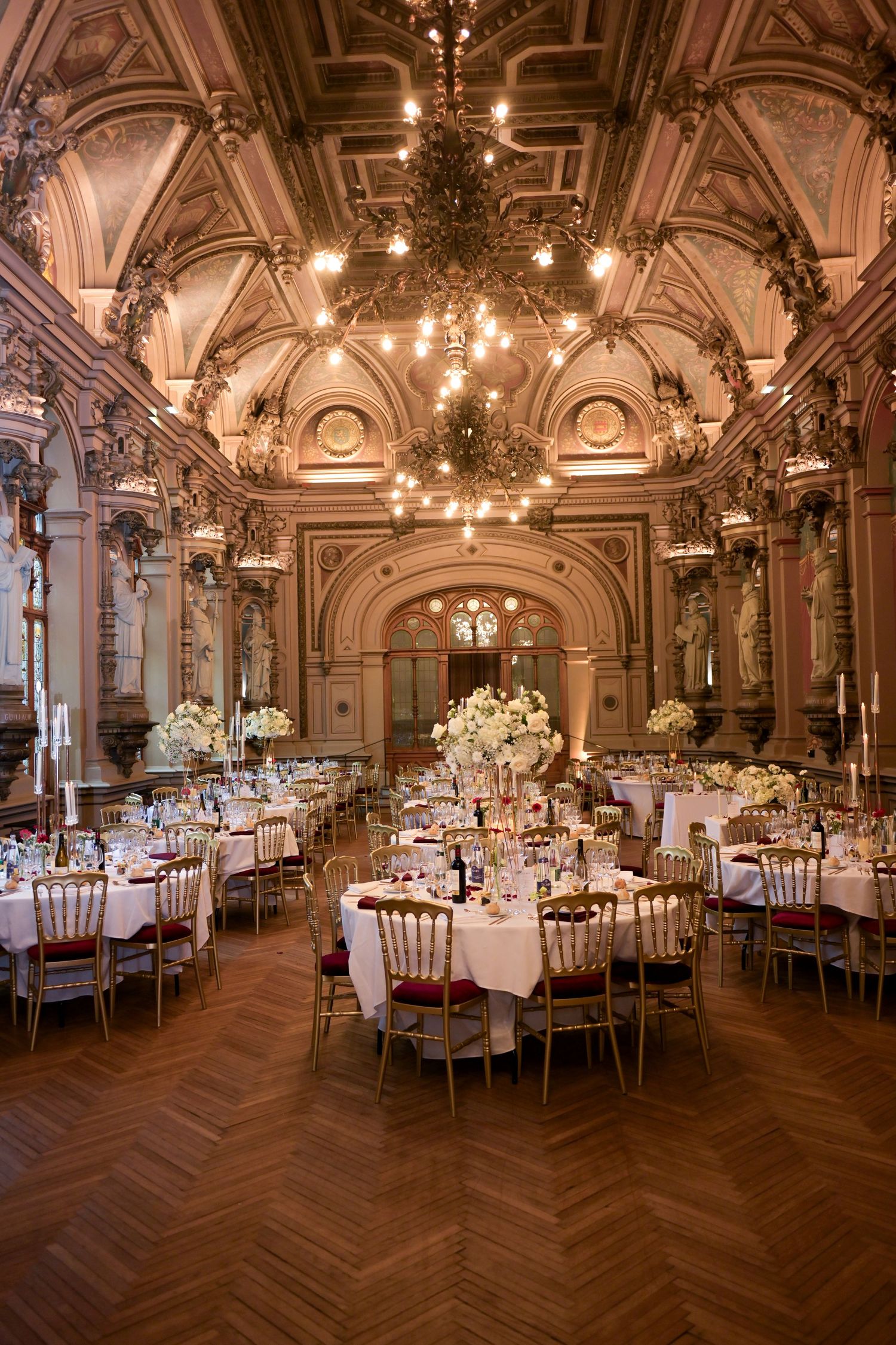 Elegant ballroom with ornate ceiling, chandeliers and round tables set for a formal reception.