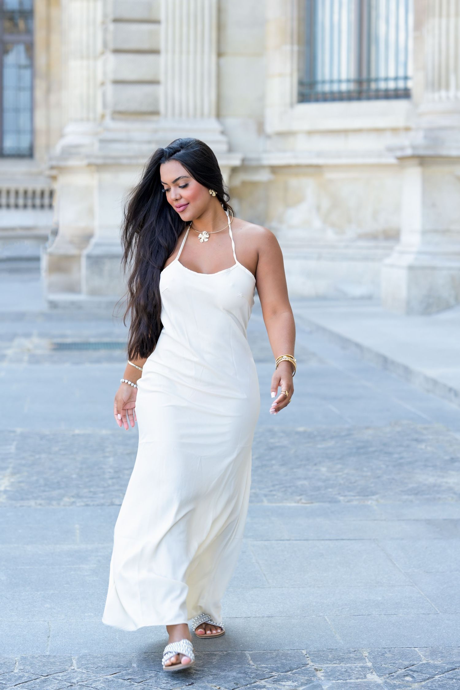 Someone wearing a white halter dress walks gracefully past classical architecture.