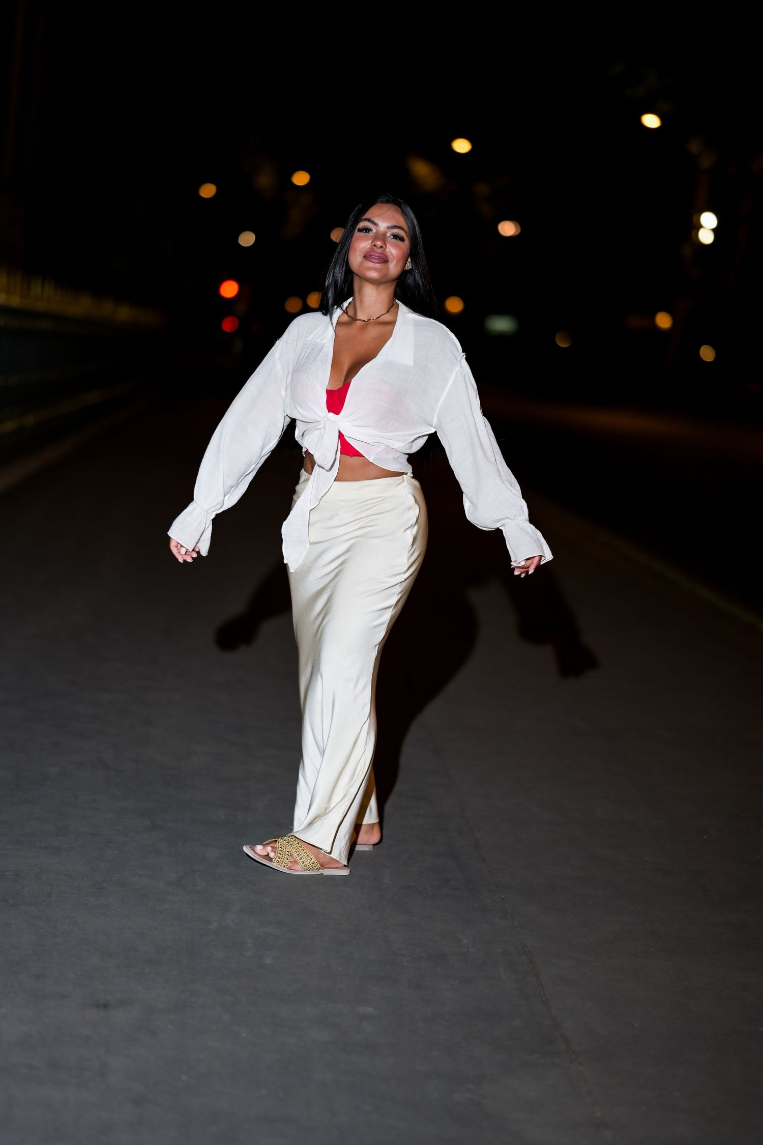 A candid street style photo of someone walking in an all-white ensemble with red accent top.