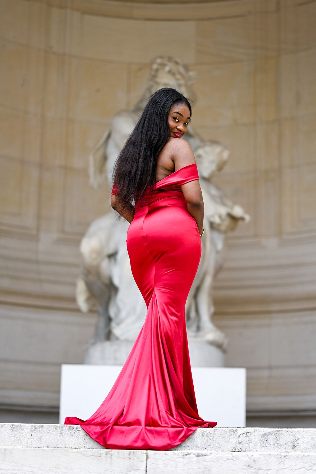 Red mermaid gown silhouette posed elegantly near classical statue display.