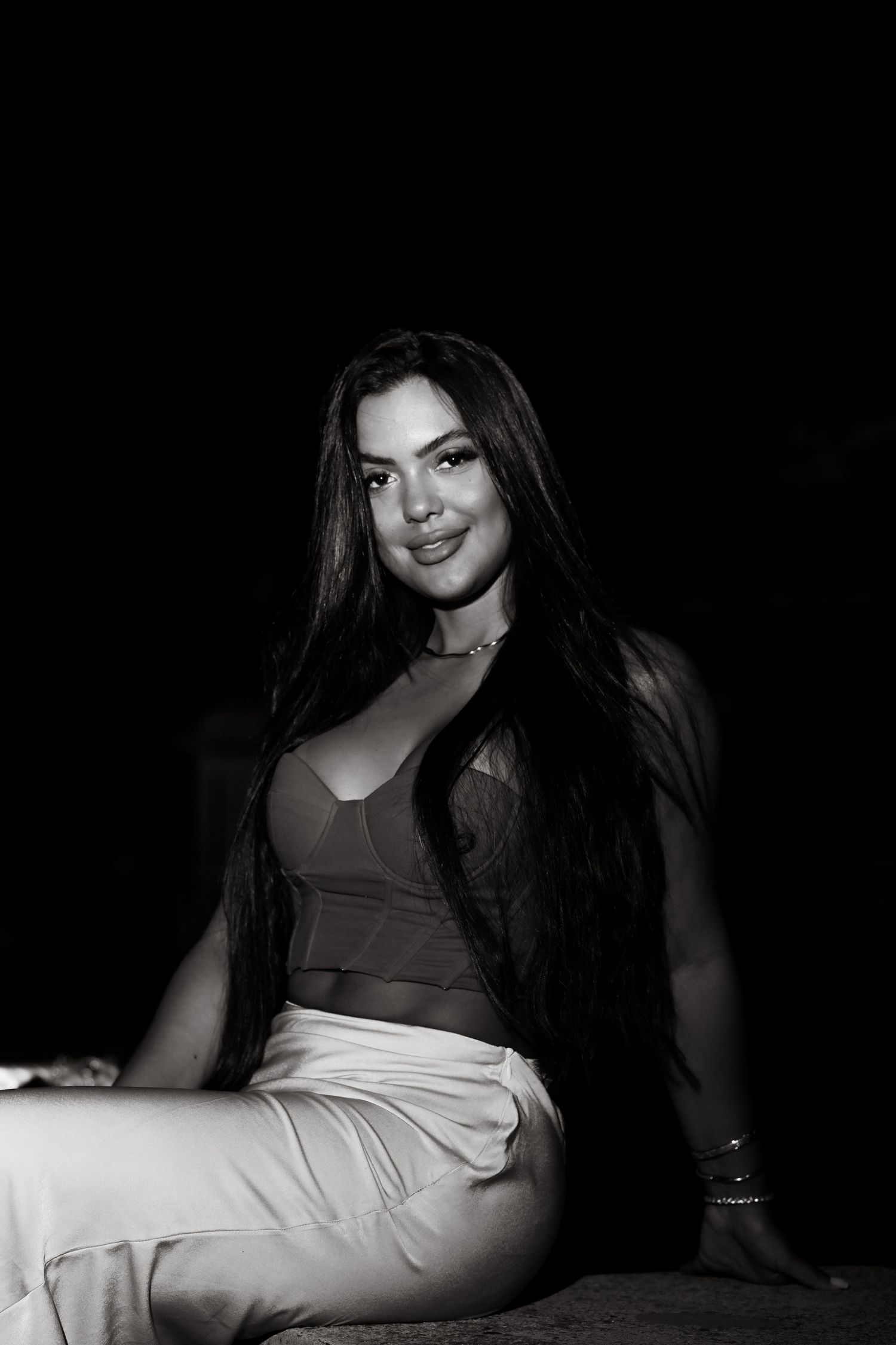 A black and white portrait of a woman with long dark hair posing in casual attire against a dark background.