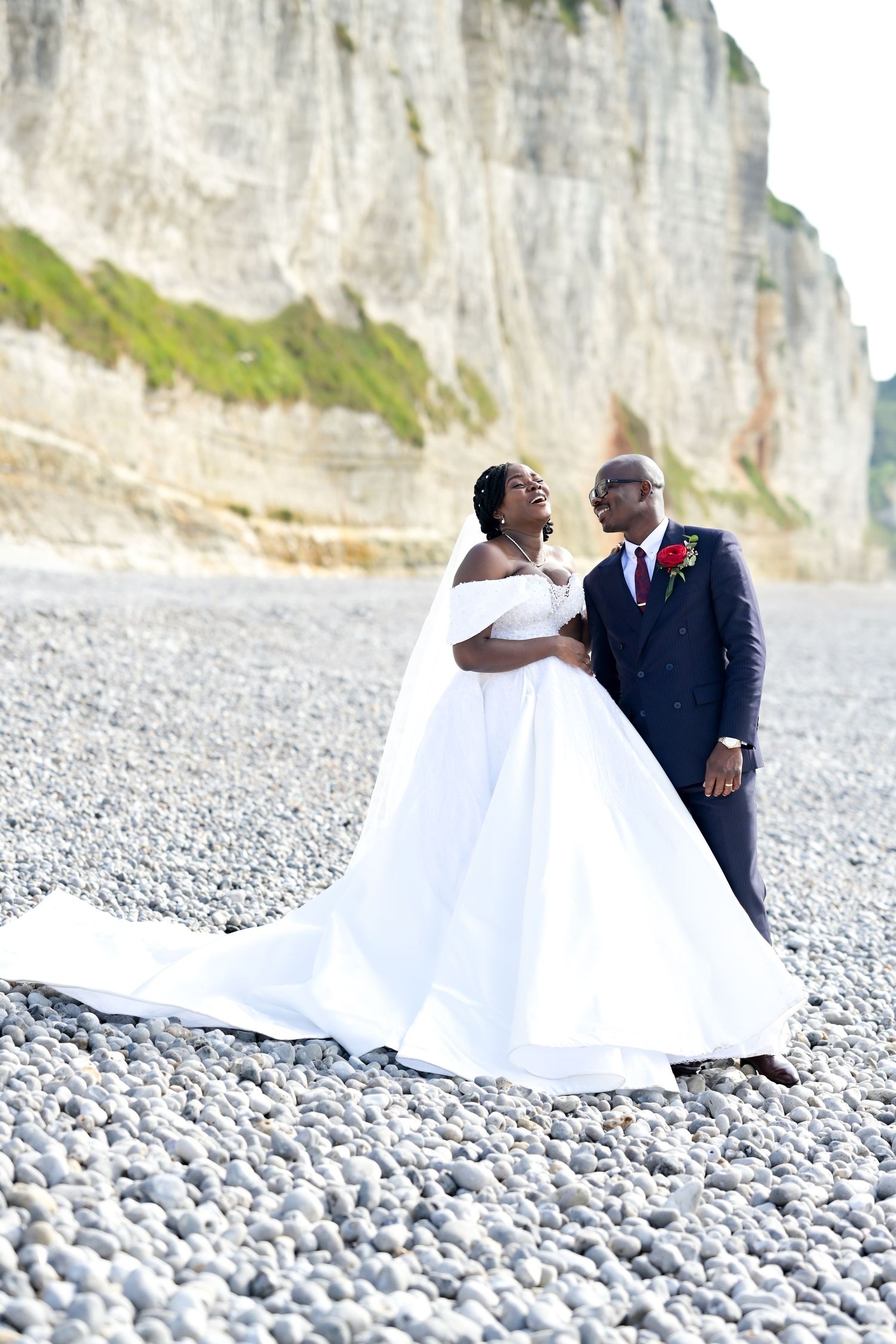 Newlyweds pose on a pebble beach with dramatic white cliffs in the background.