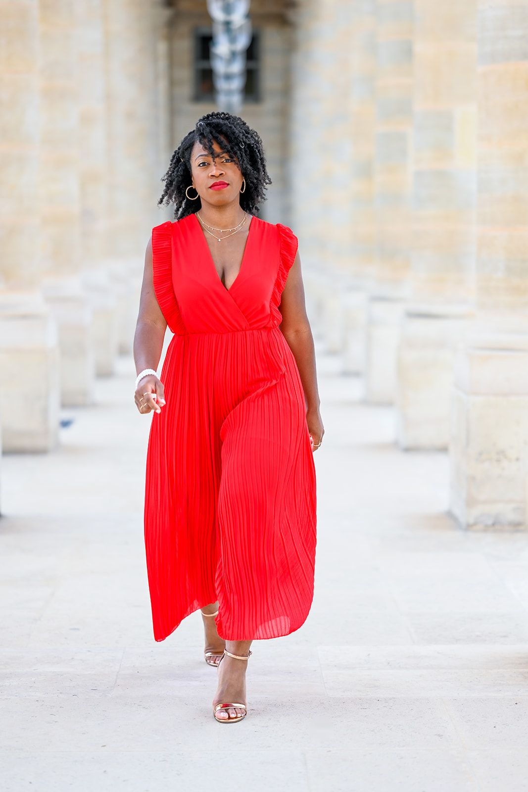 Flowing red pleated dress captured in motion against stone architecture.