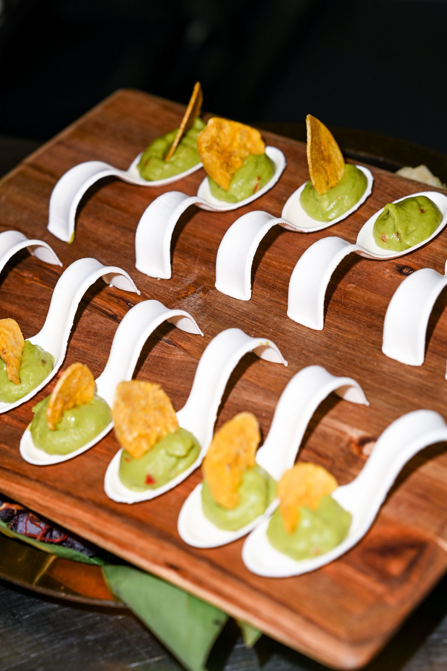Elegant appetizers served on white ceramic spoons arranged on wooden board.